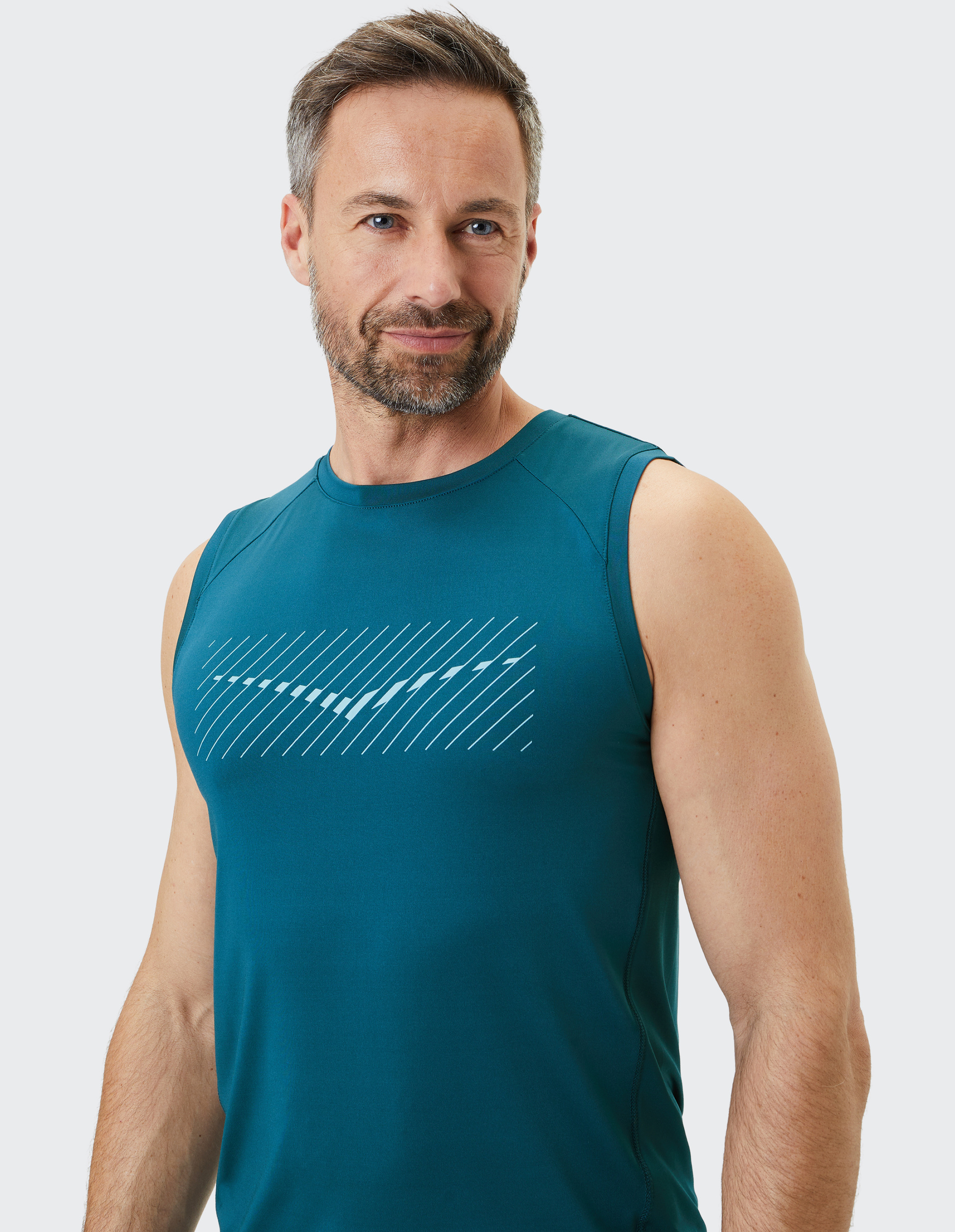 Ein Mann mit Bart trägt ein ärmelloses, türkisfarbenes Sportshirt mit diagonalen Streifen, vor neutralem Hintergrund.