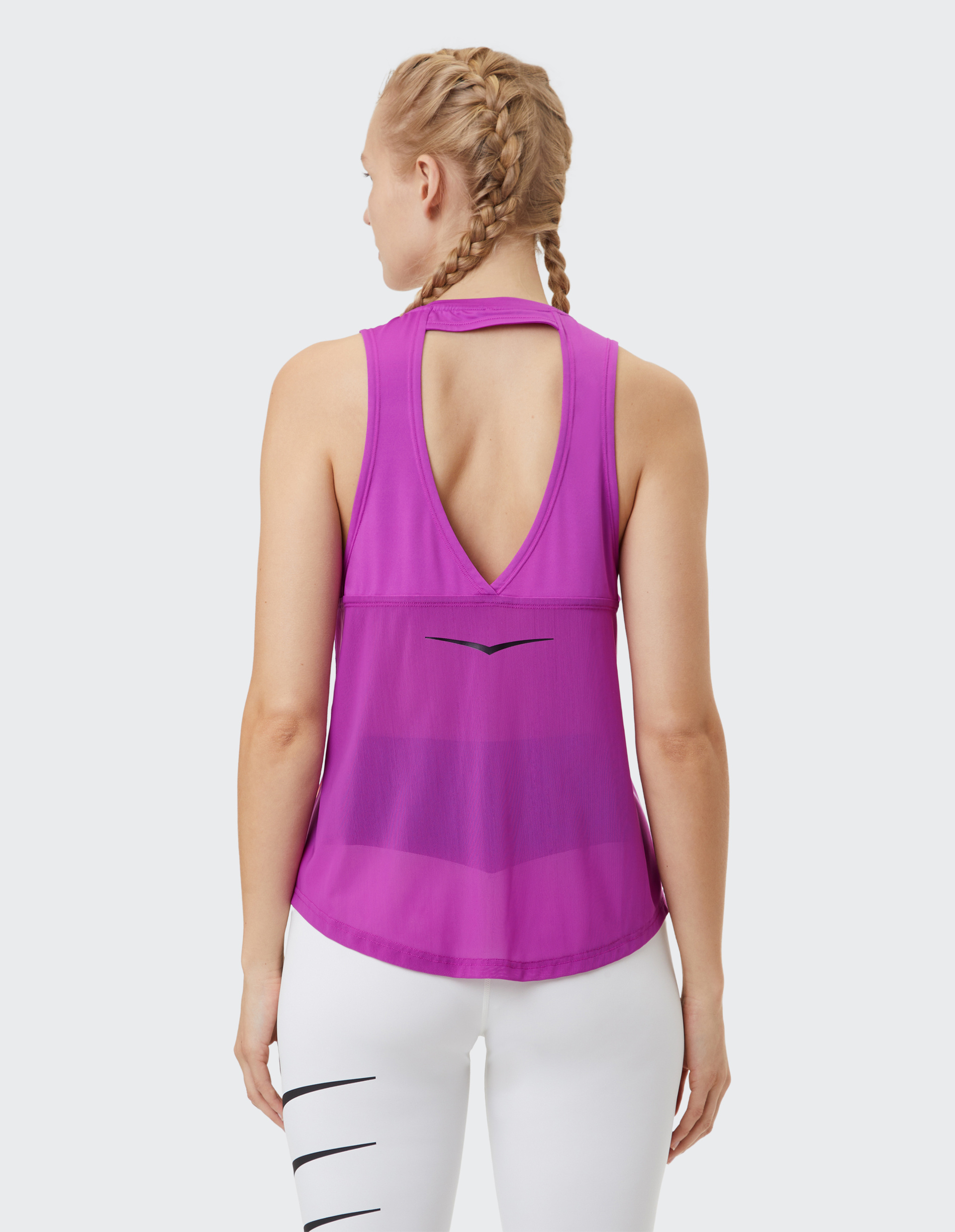 Eine Person mit geflochtenem Haar trägt ein ärmelloses, violettes Oberteil mit tiefem Rückenausschnitt und weiße Leggings.