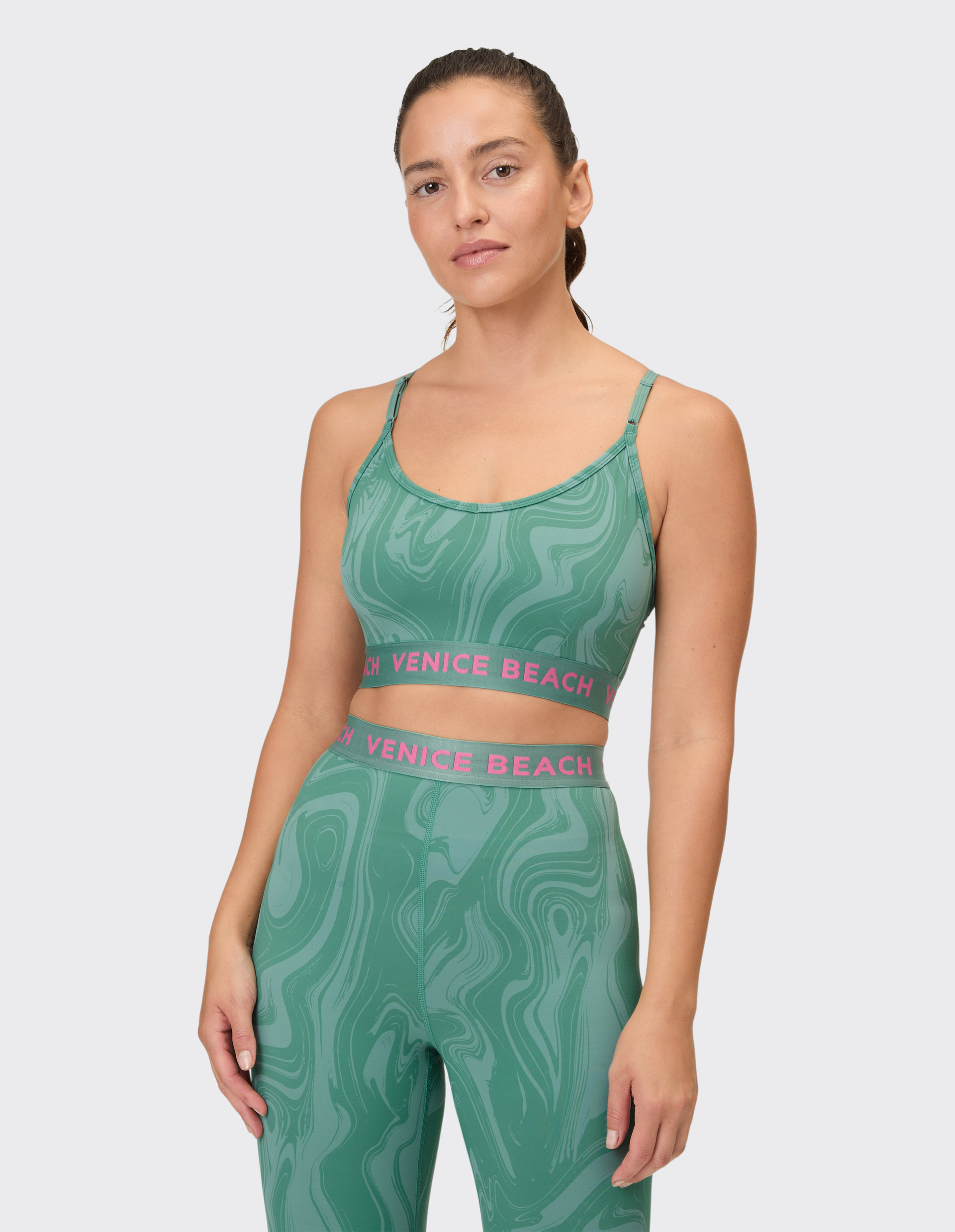 Eine Frau trägt einen grünen Sport-BH mit marmoriertem Muster und BH-Trägern, der mit einem gleichfarbigen Unterteil kombiniert wird.