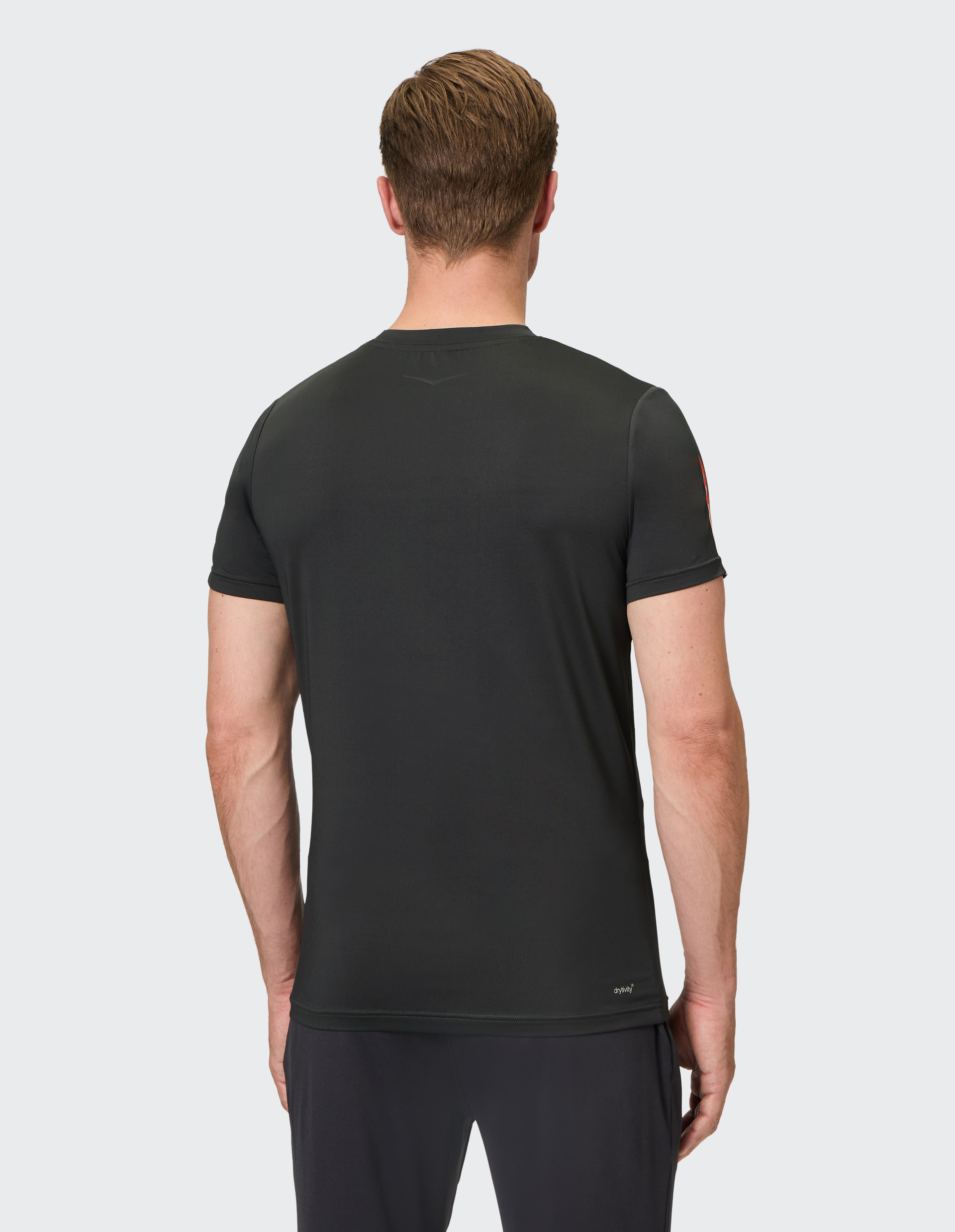 Ein Mann mit kurzen Haaren trägt ein schwarzes T-Shirt von hinten gesehen, vor einem hellgrauen Hintergrund.