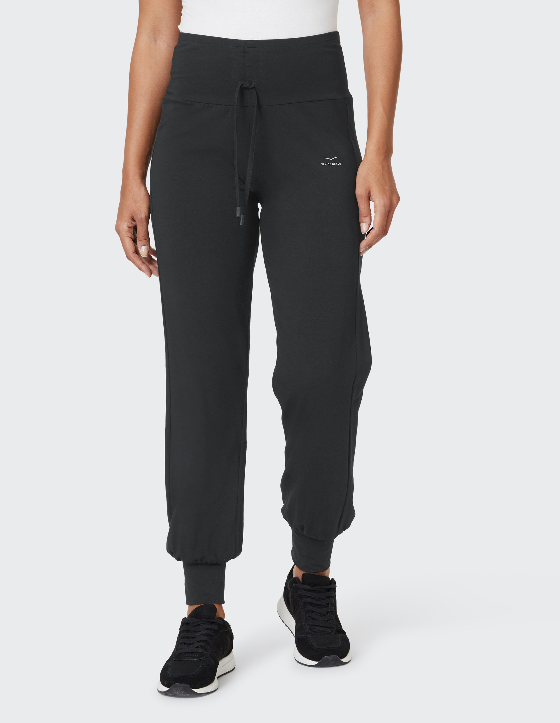 Eine Person trägt eine schwarze Jogginghose mit Kordelzug, kombiniert mit schwarzen Turnschuhen und einem weißen Oberteil.