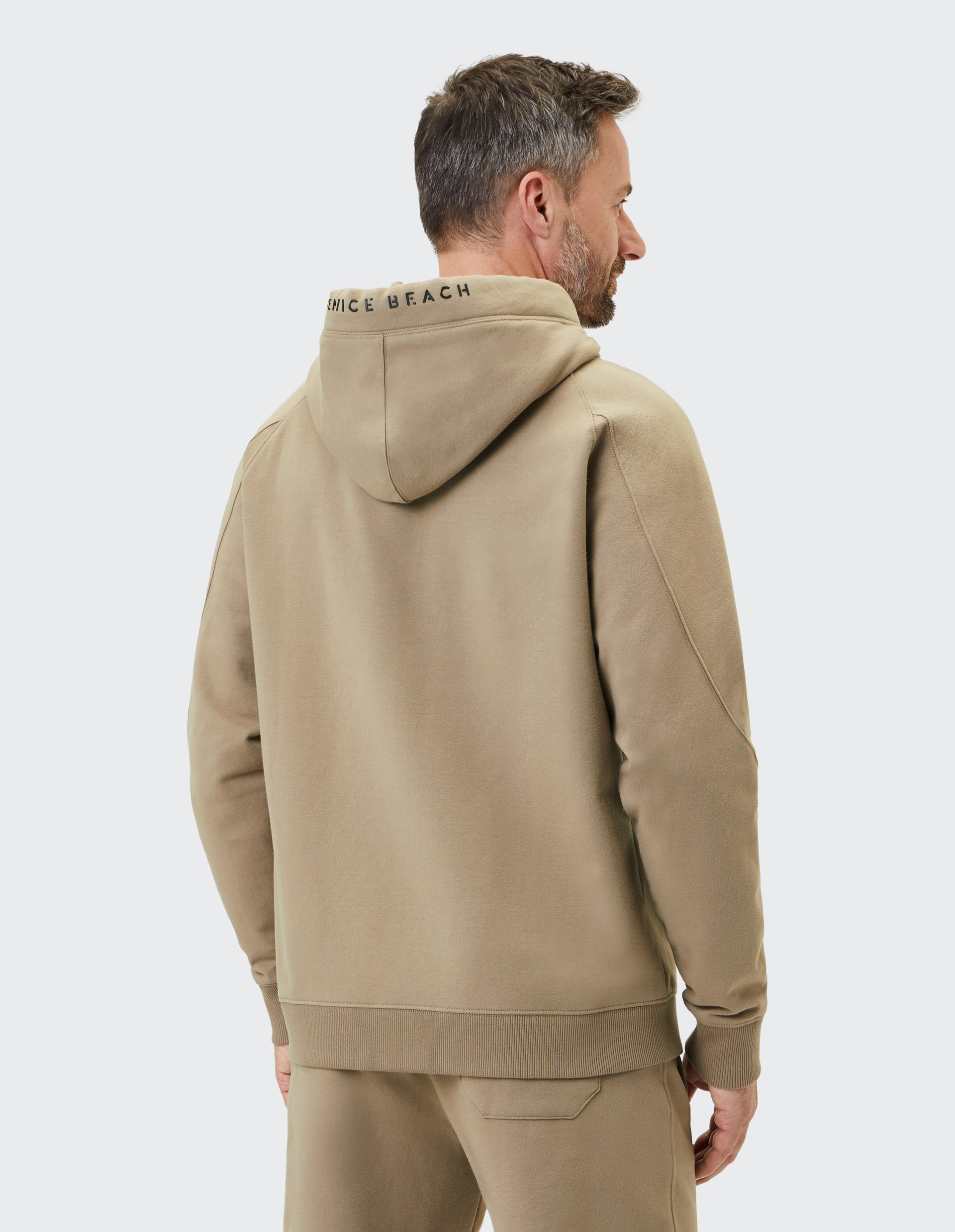 Beiger Kapuzenpullover mit Reißverschluss, Kängurutaschen und Kordelzügen an der Kapuze, markiert mit einem kleinen Logo links auf der Brust.