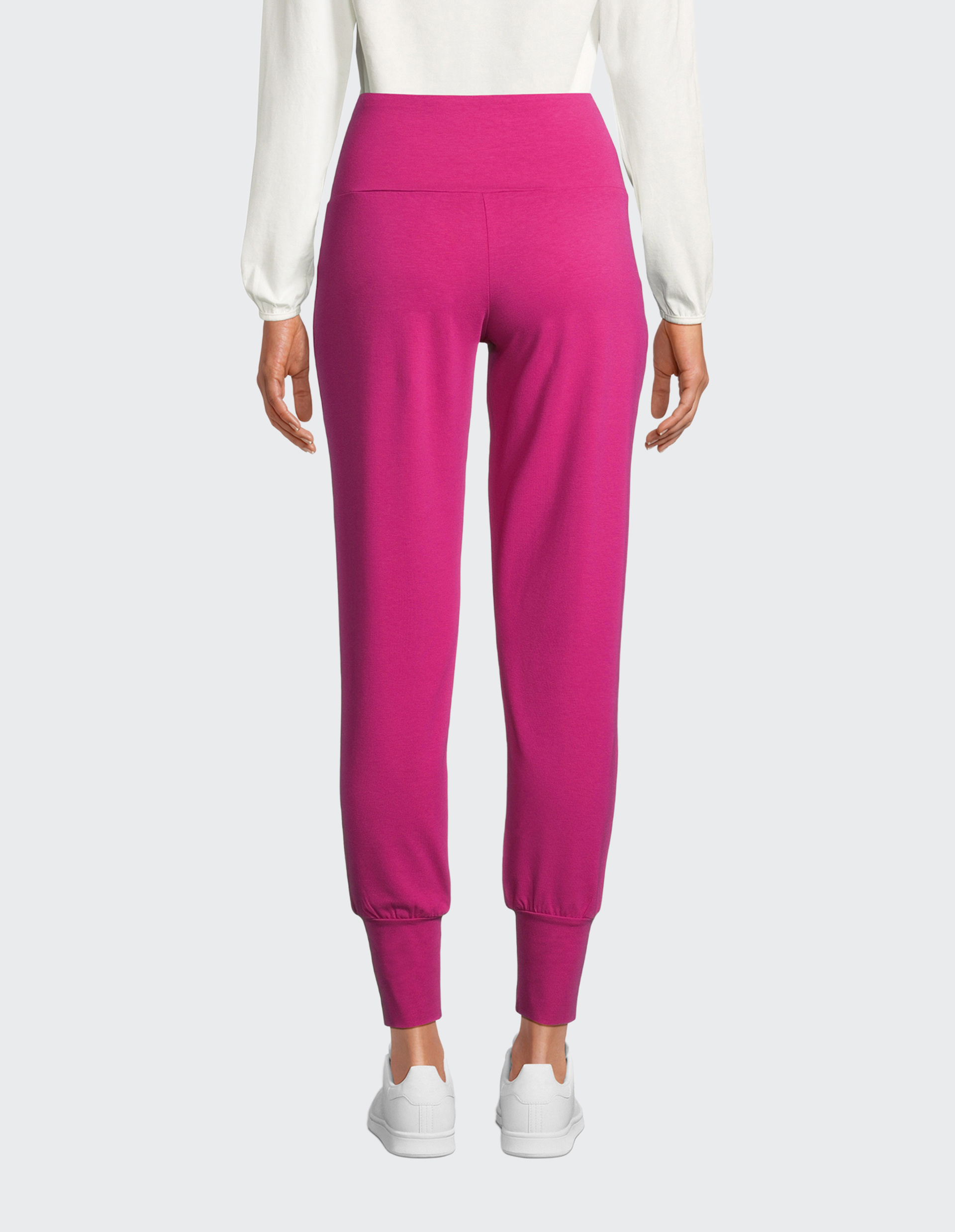 Eine Person trägt eine langärmlige weiße Bluse und eine auffällige fuchsiafarbene Hose mit Bündchen und elastischem Bund.