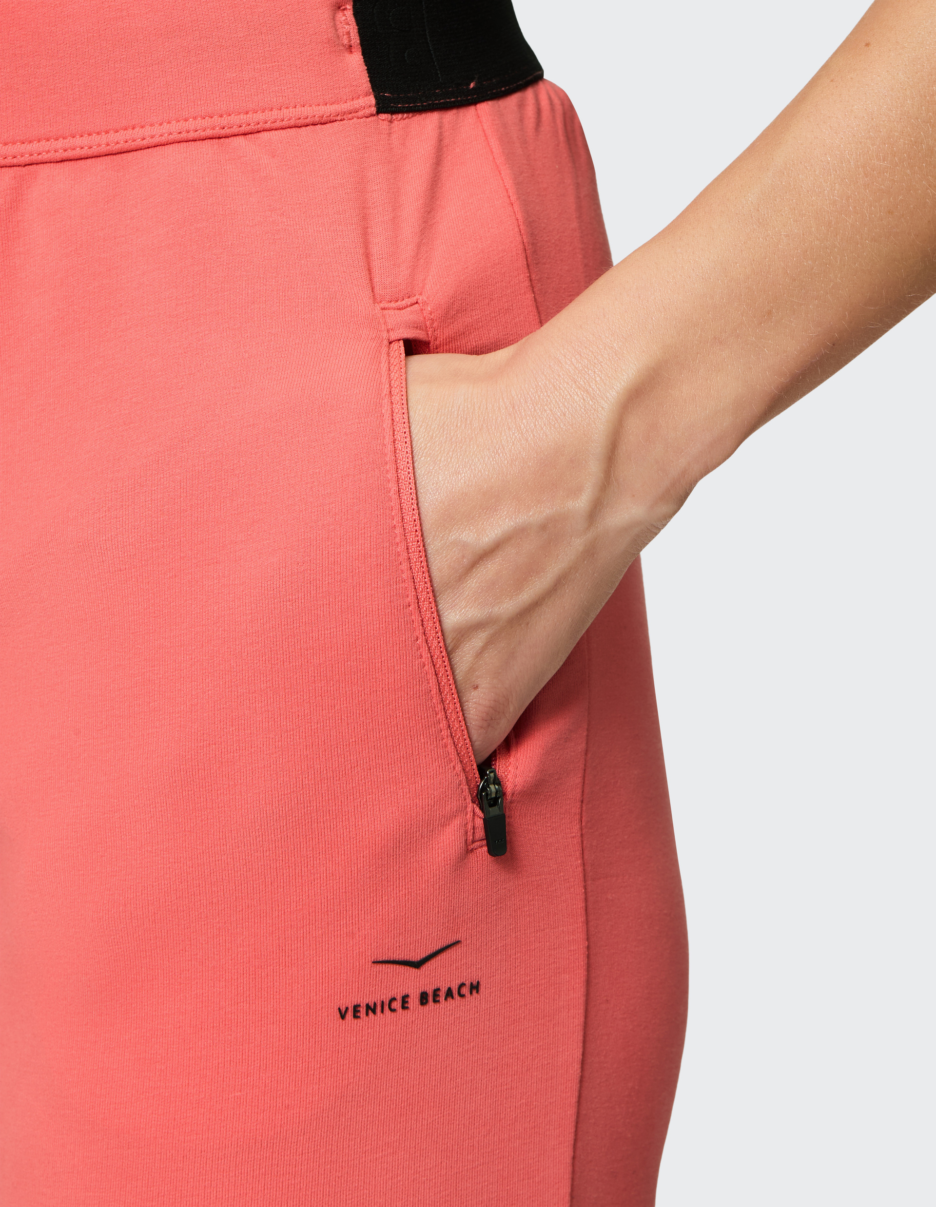Nahaufnahme einer Hand in einer Reißverschlusstasche einer rosafarbenen Sporthose mit "Venice Beach"-Logo.