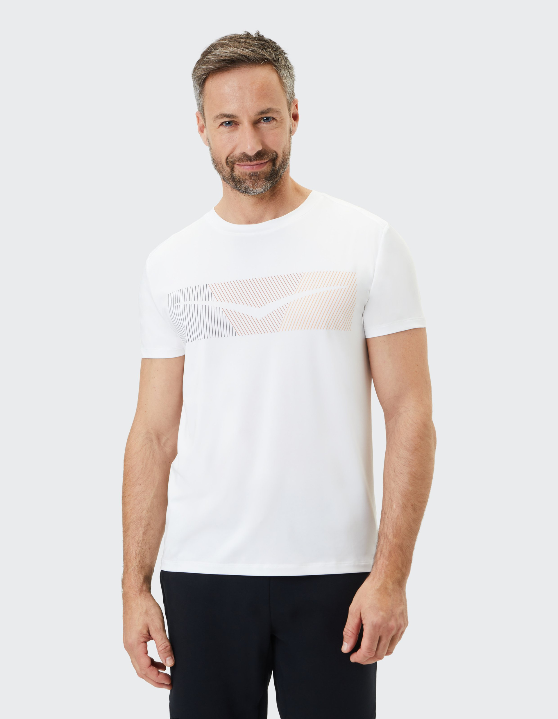 Ein Mann mit Bart und grauem Haar trägt ein weißes T-Shirt mit linearem Muster und blickt freundlich in die Kamera vor neutralem Hintergrund.