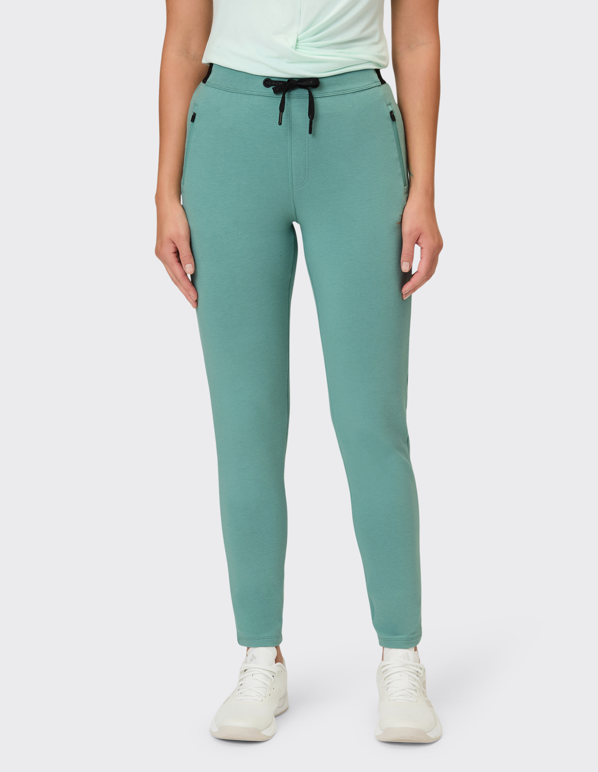Eine Frau trägt schlichte, mintgrüne Jogginghosen mit seitlichen Reißverschlusstaschen und einem schwarzen Kordelzug am Bund.