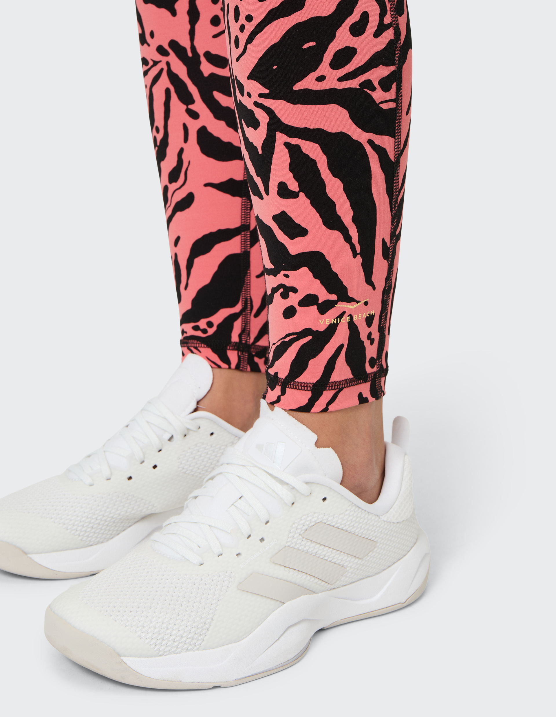 Weiße Sneaker auf hellgrauem Boden, kombiniert mit rosa Leggings mit schwarzem, abstraktem Blumenmuster, aus der Venice Beach Kollektion.