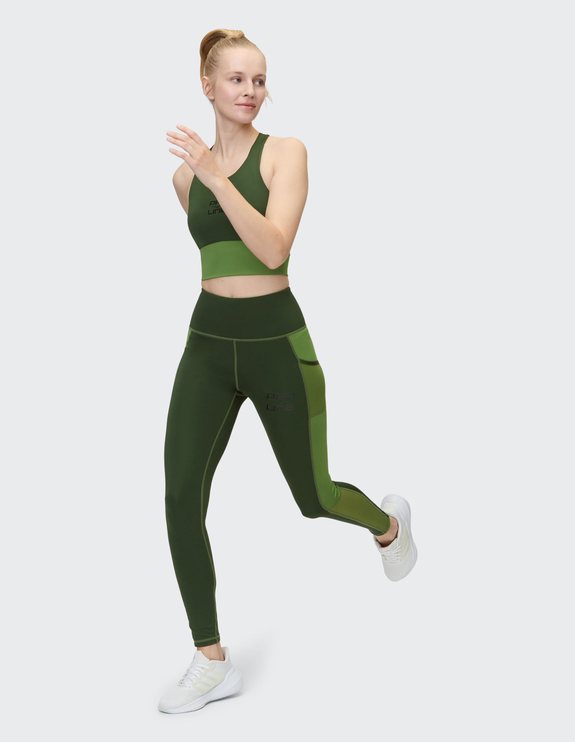 Person in grüner Sportkleidung joggt, trägt weiße Turnschuhe und hat die Haare zu einem Knoten hochgebunden.