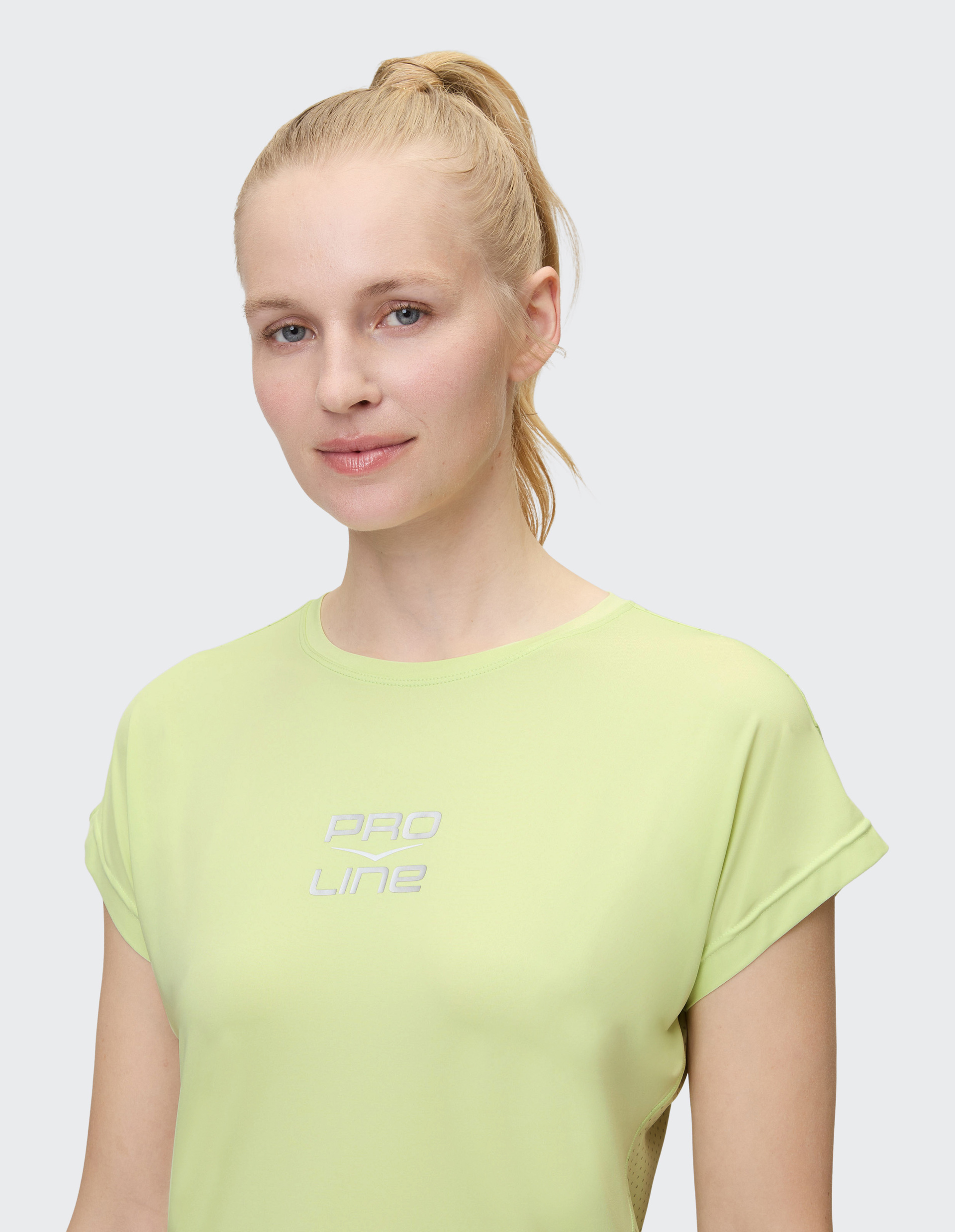 Eine Person mit blondem Pferdeschwanz trägt ein hellgrünes T-Shirt mit der Aufschrift "Pro Line" und blickt freundlich in die Kamera.
