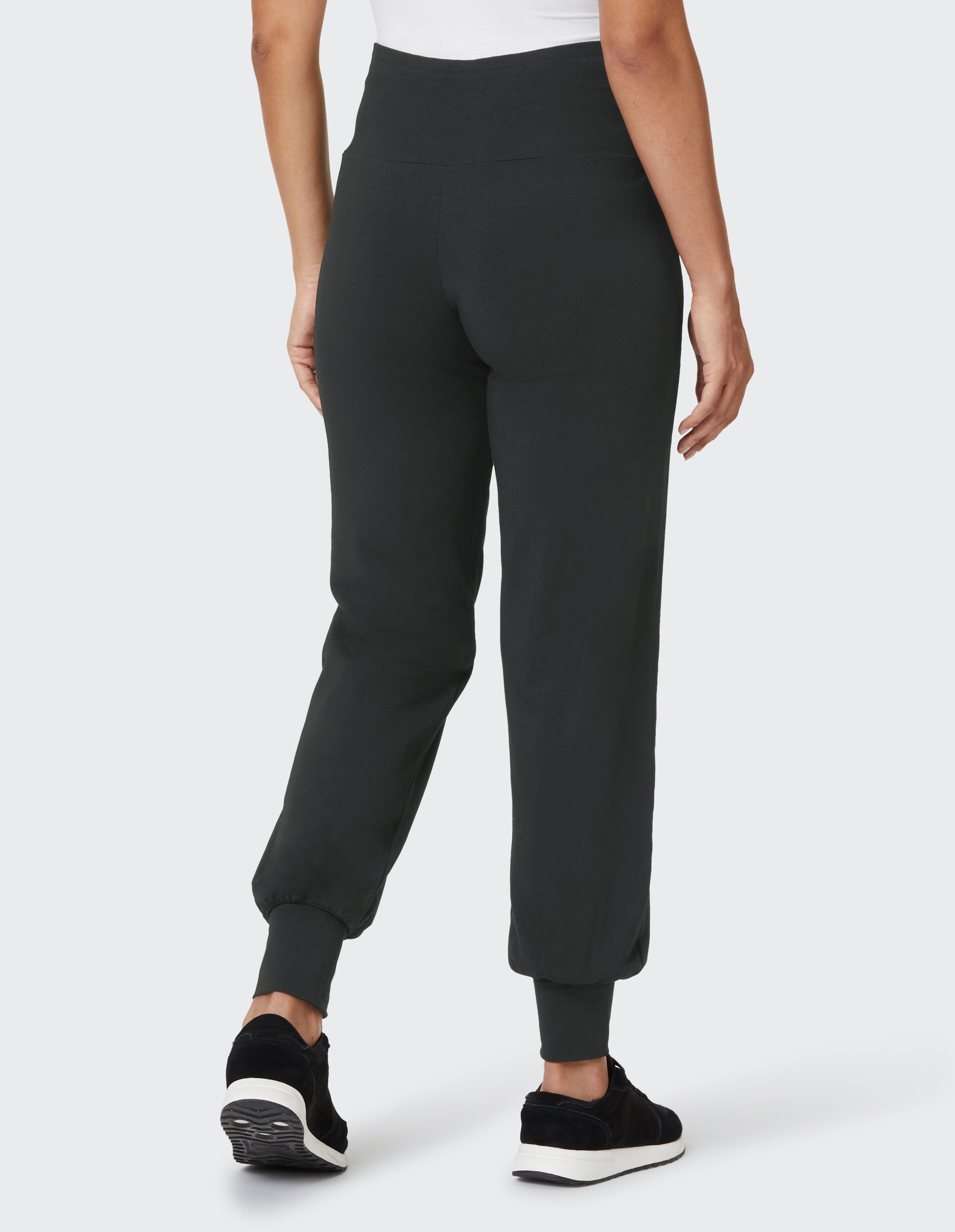 Person trägt schwarze Jogginghose und schwarze Sneaker; Ansicht von hinten, Hosenbein endet in elastischem Bündchen.