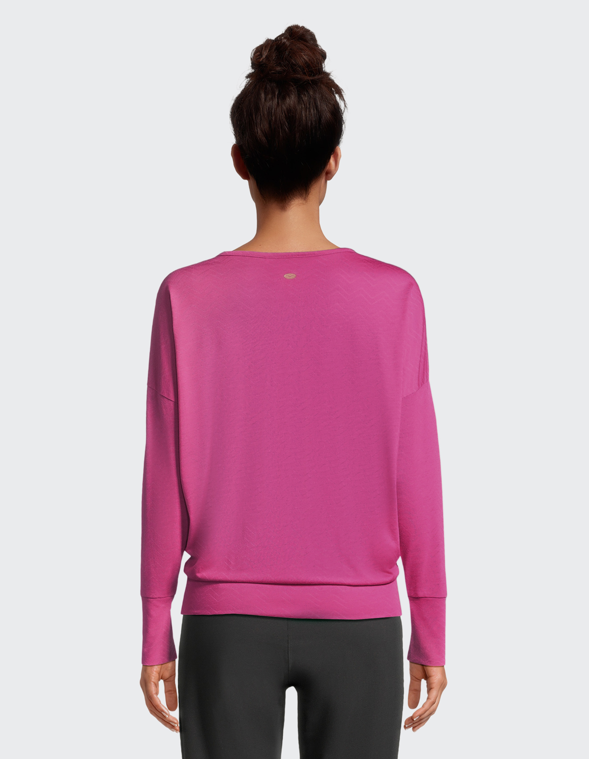 Eine Person mit Dutt trägt einen pinken Pullover und schwarze Leggings, fotografiert von hinten vor grauem Hintergrund.