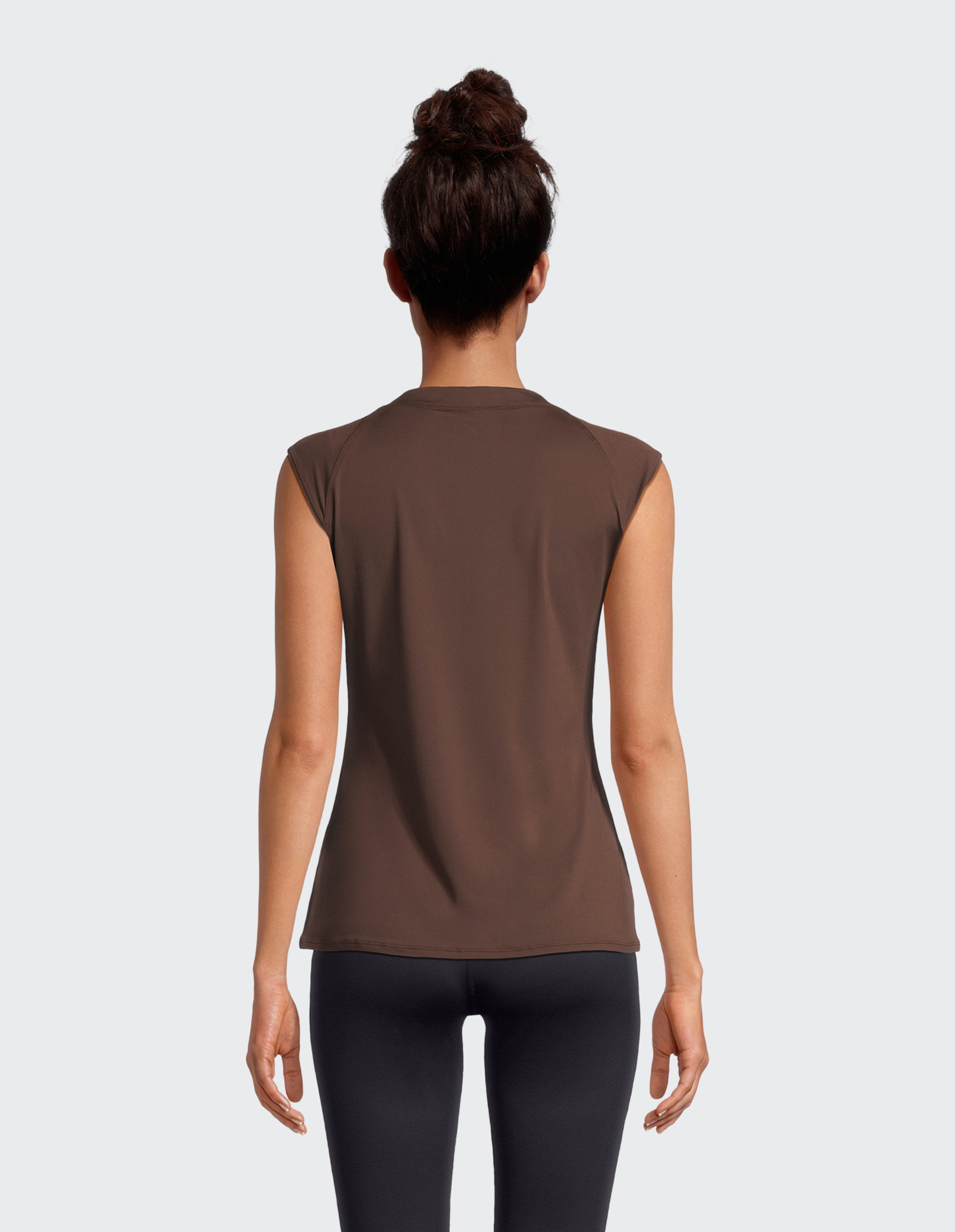 Eine Frau trägt ein braunes, ärmelloses Oberteil mit Rundhalsausschnitt und schwarze Leggings.