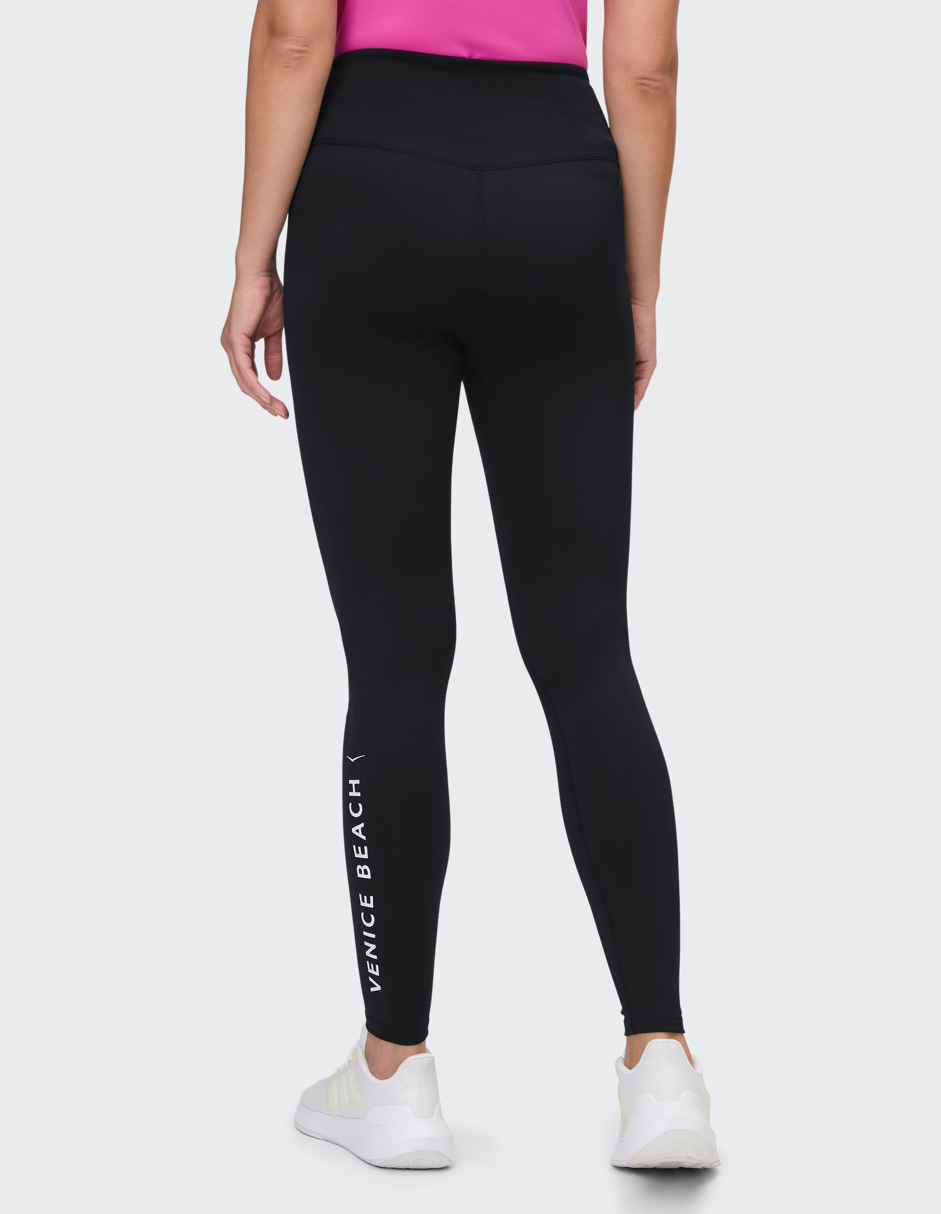 Rückansicht einer Person in schwarzer Leggings mit "VENICE BEACH" Schriftzug, pinkem Oberteil und weißen Sportschuhen.