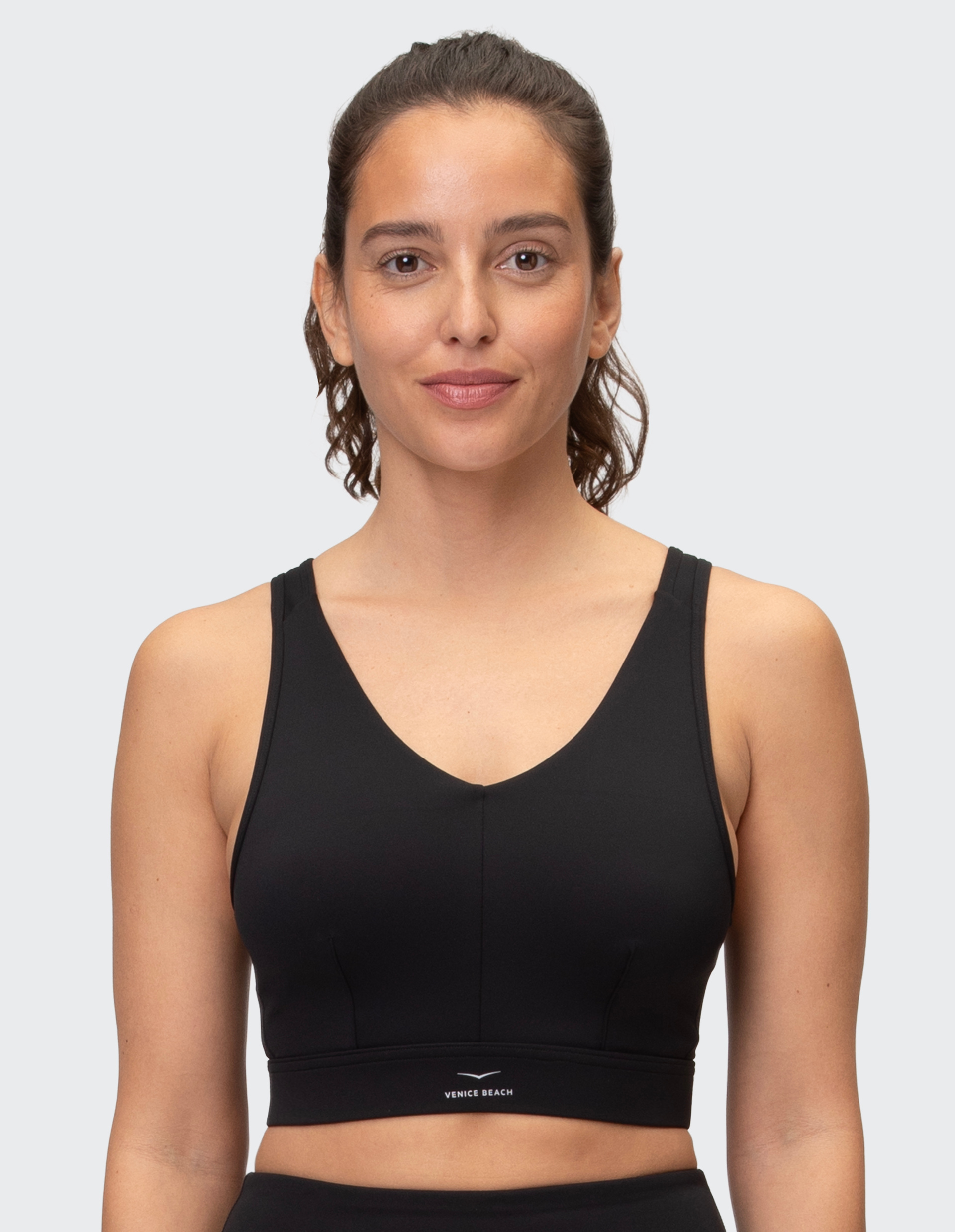Eine Frau mit lockigem Haar trägt ein schwarzes Sporttop und lächelt leicht vor einem weißen Hintergrund.