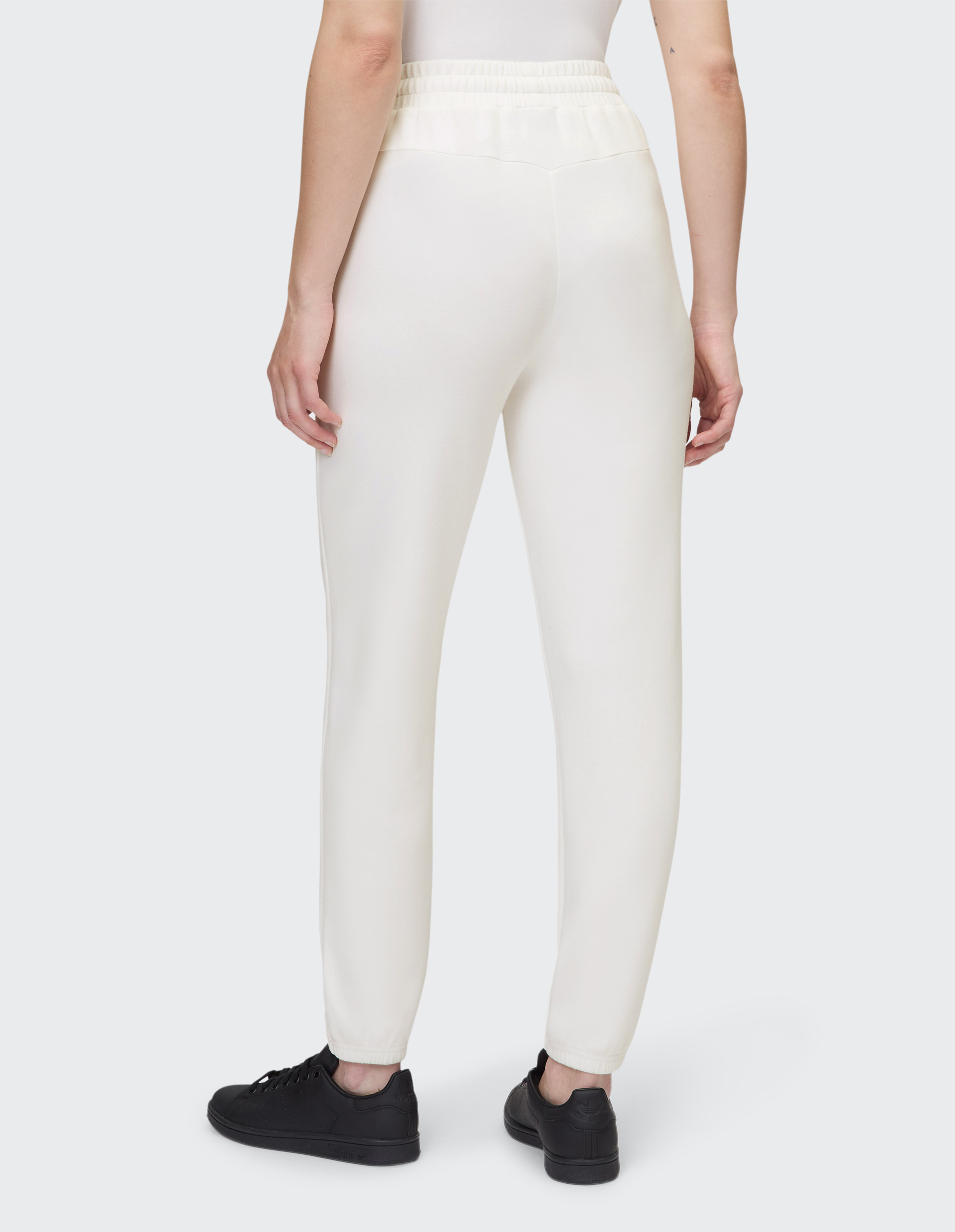 Eine Person trägt eine weiße Jogginghose mit elastischem Bund, kombiniert mit schwarzen Sneakers, von hinten fotografiert.