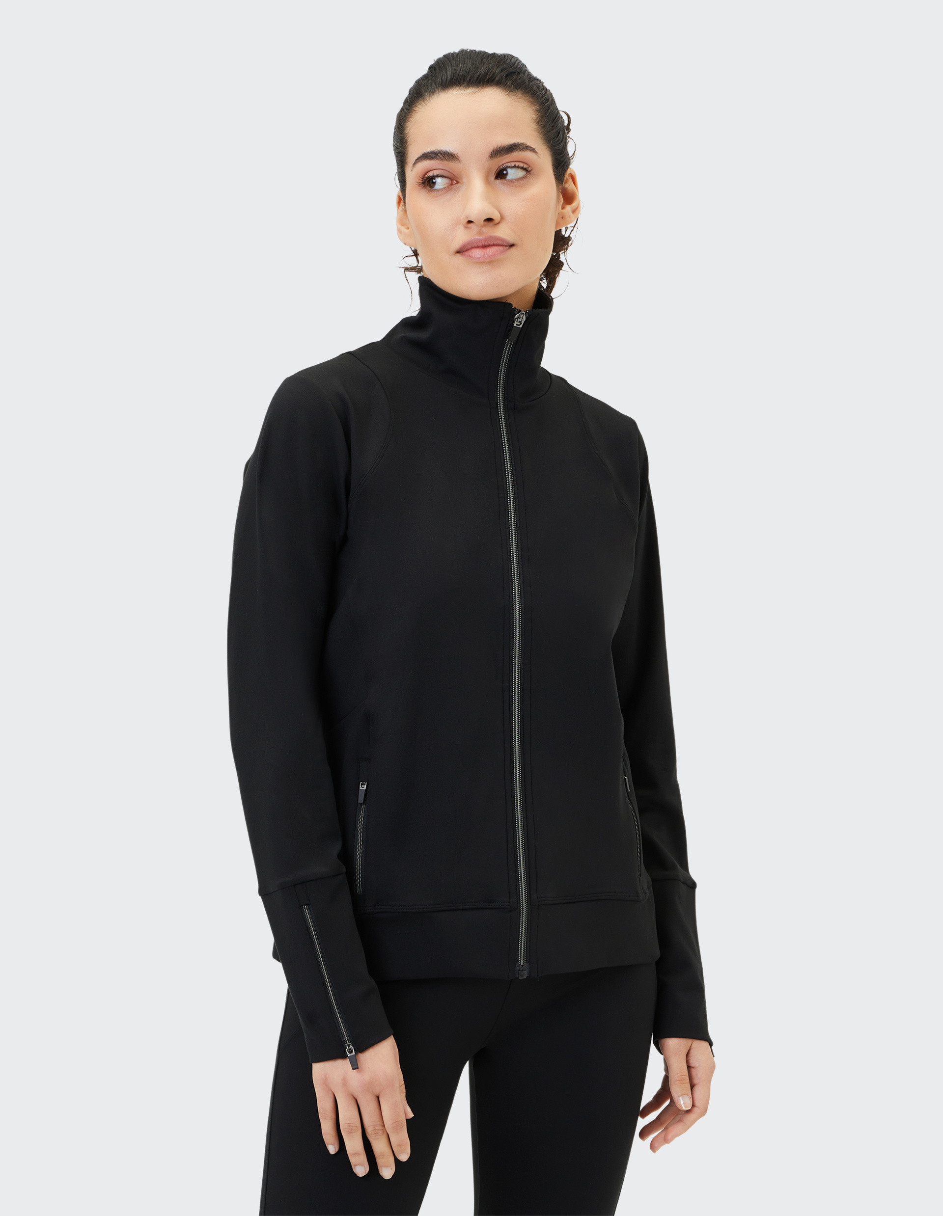 Eine Person trägt eine schwarze Jacke mit Reißverschluss, steht im Profil und blickt nach rechts vor einem hellen Hintergrund.