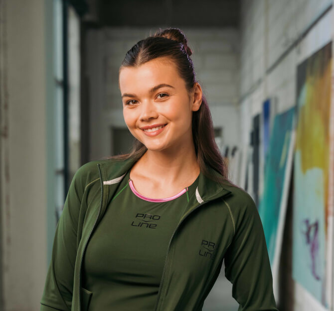 Frau mit braunen Haaren im dunkelgrünem Sportoutfit der Marke Venice Beach.