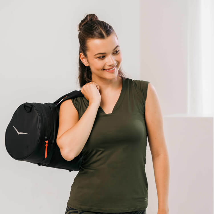 Frau in dunkelgrünem Top und einer über die Schulter hängenden schwarzen Sporttasche.