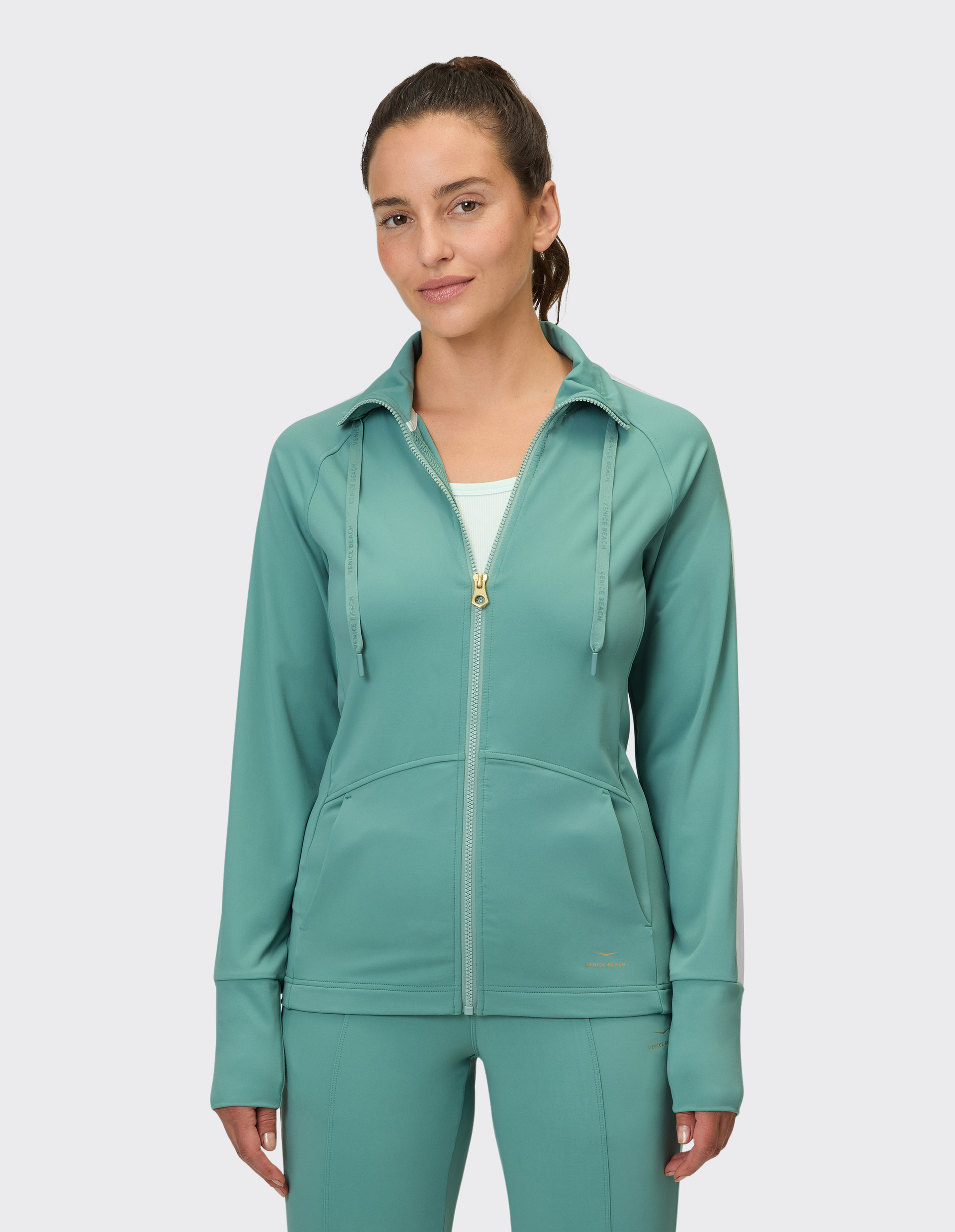 Eine Frau trägt eine smaragdgrüne Reißverschlussjacke und passende Hosen, die ein bequemes Outfit bilden.