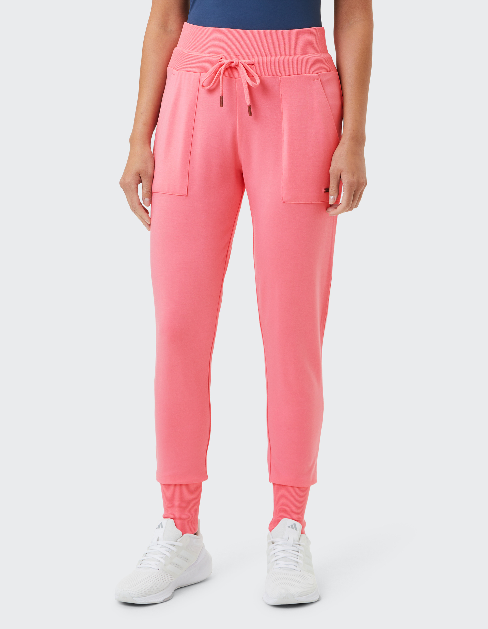 Person trägt eine rosa Jogginghose mit Kordelzug, zwei Taschen und weißem Sneaker auf hellem Hintergrund, Oberteil ist dunkelblau.