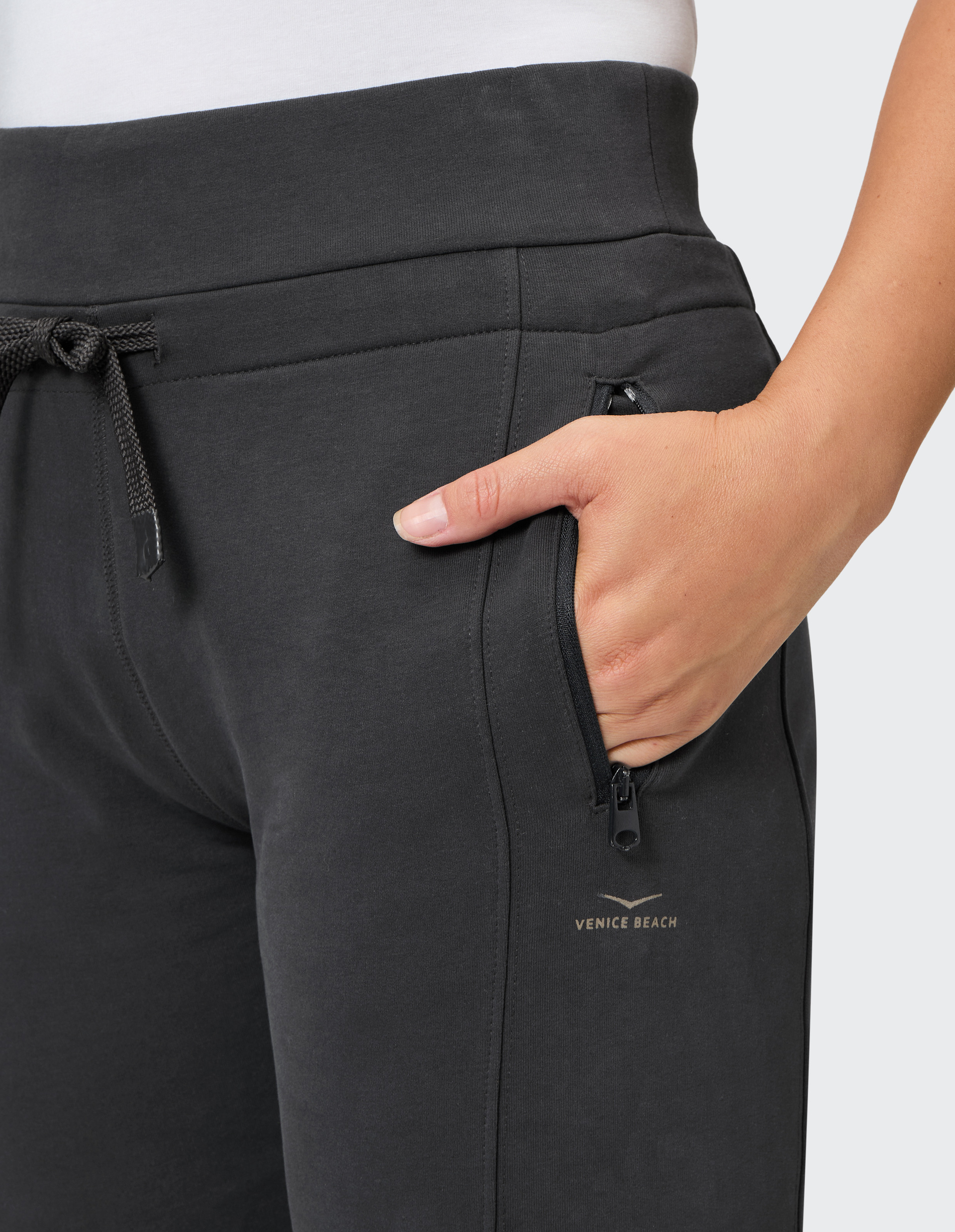 Schwarze Sporthose mit Taschenreißverschluss, einer Hand in der Tasche und einem kleinen weißen Logo nahe dem Oberschenkel.