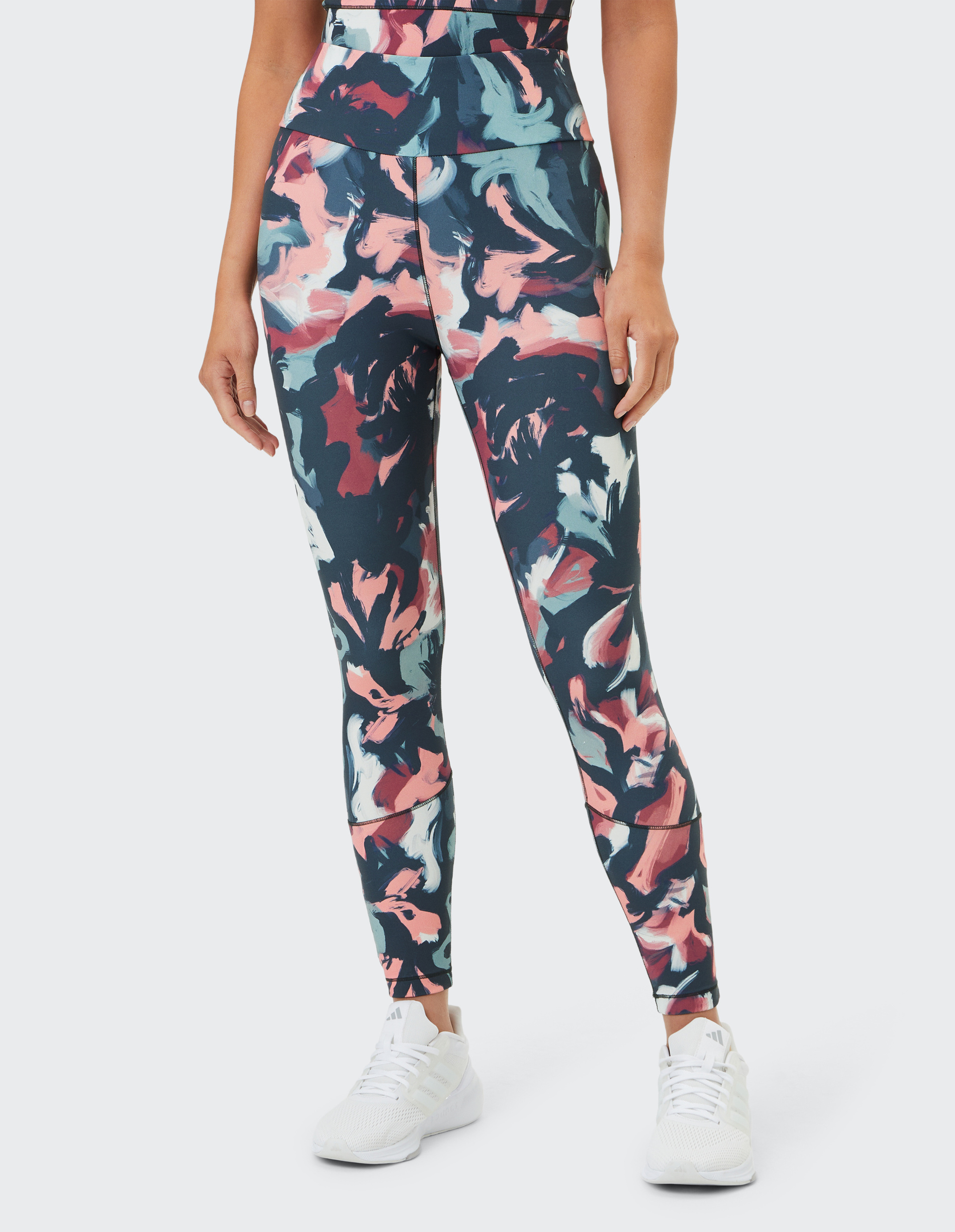 Frau trägt Leggings mit abstraktem, buntem Muster aus Blau-, Rosa- und Weißtönen, dazu weiße Turnschuhe; sportlicher Look.