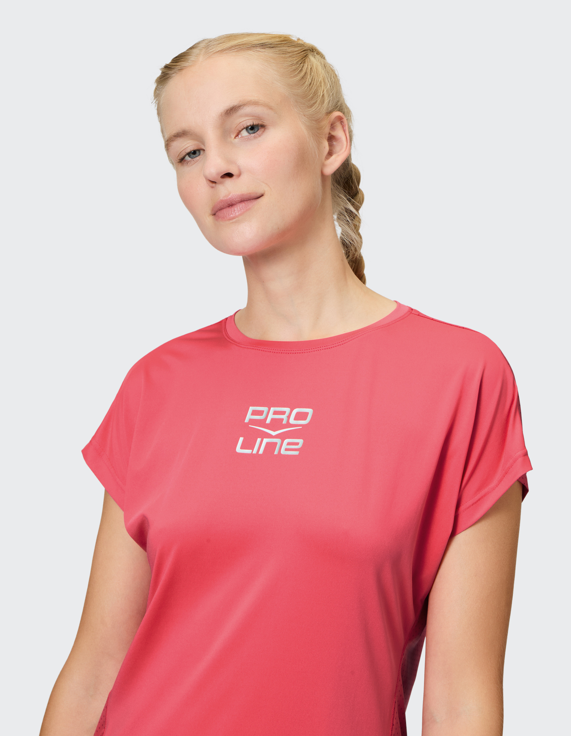 Frau mit geflochtenem, blondem Haar trägt ein pinkes Shirt mit PRO LINE-Aufdruck; sie lächelt leicht und schaut selbstbewusst.