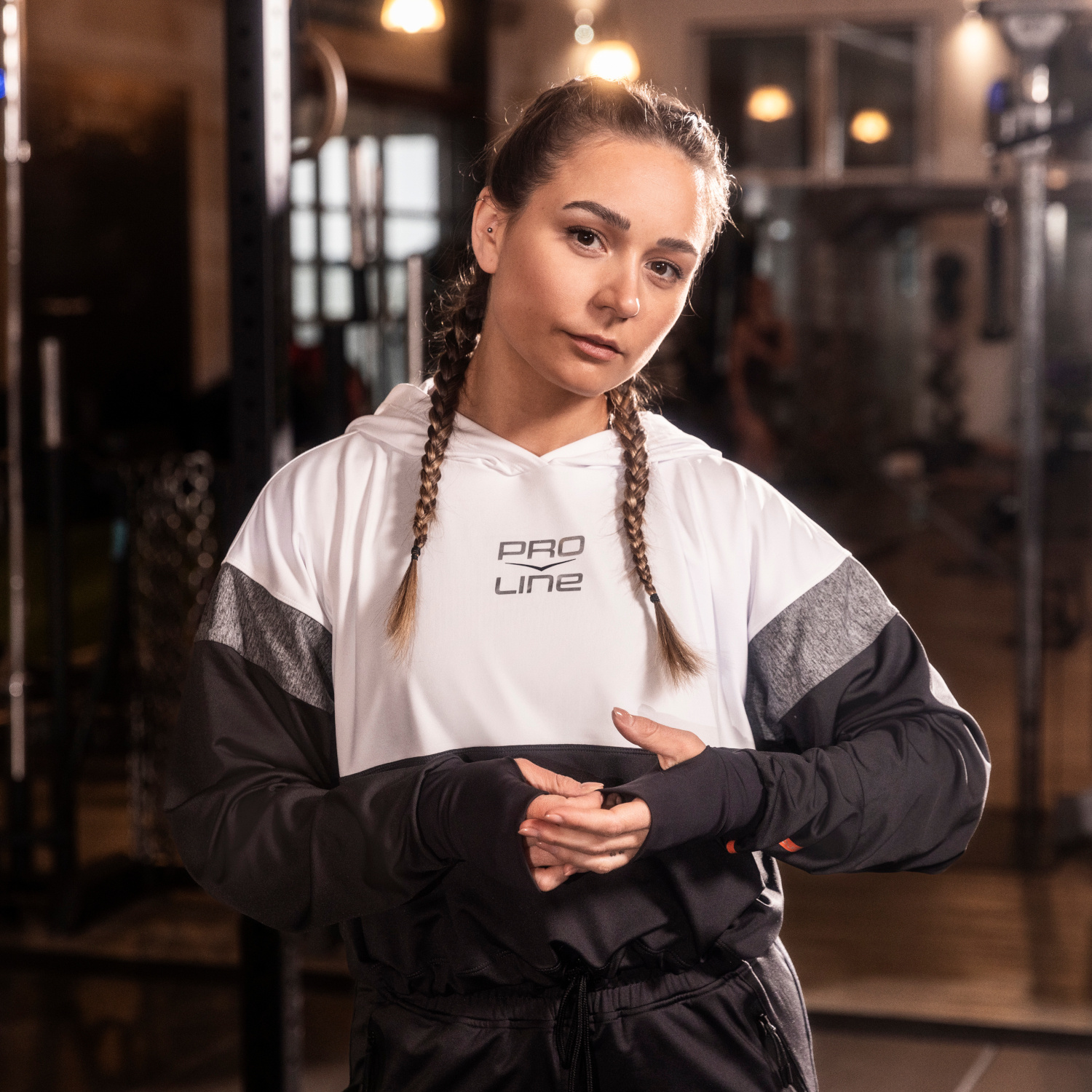 Eine Frau in Sportkleidung  schaut frontal in die Kamera und zupft an ihrem Pullover Ärmel.