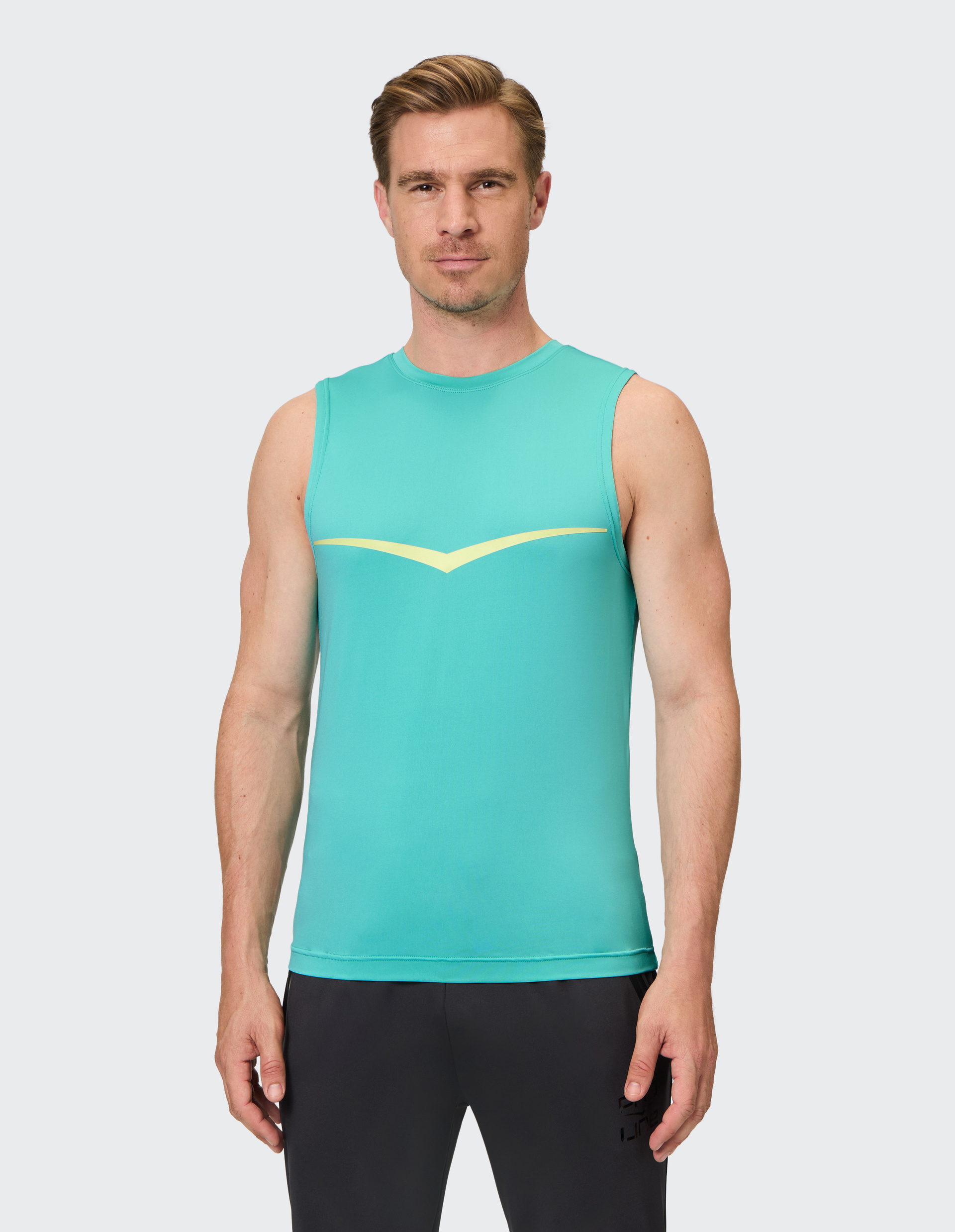 Mann in türkisfarbenem ärmellosem Sportshirt mit gelber Linie, schwarzer Hose, neutrale Miene, heller Hintergrund.