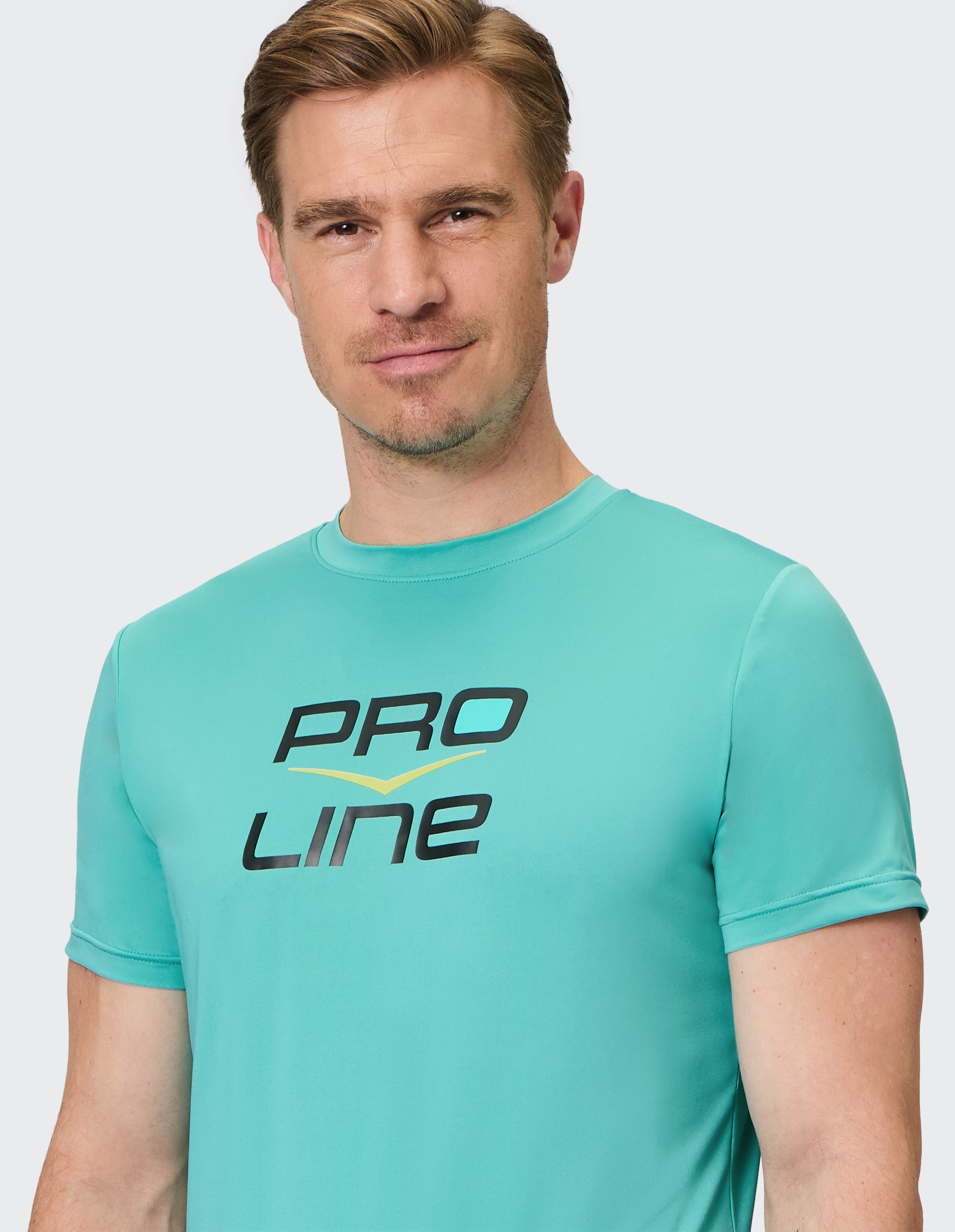 Ein Mann in einem türkisfarbenen T-Shirt mit der Aufschrift "PRO LINE" lächelt leicht vor einem neutralen Hintergrund.