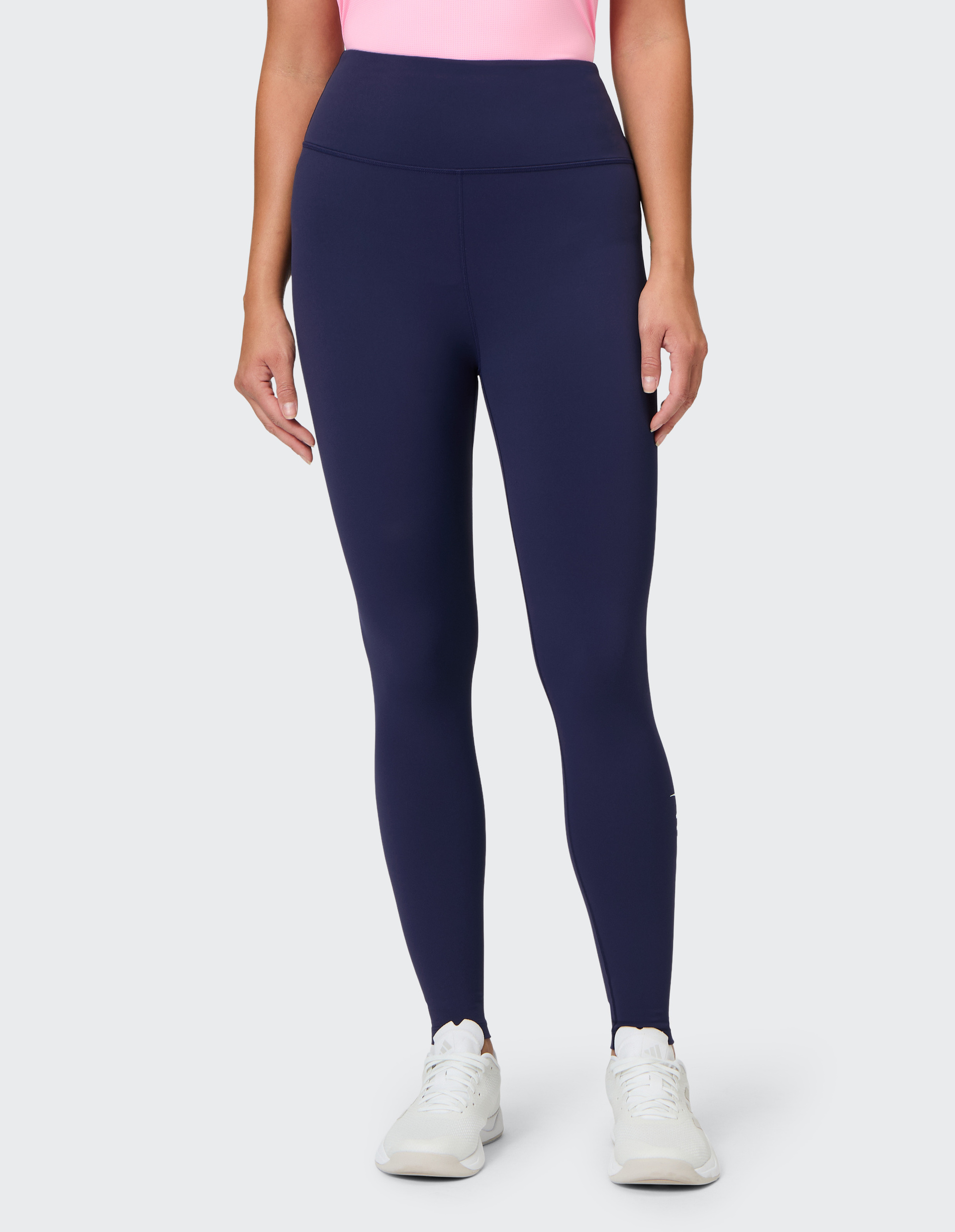 Eine Person trägt eine dunkelblaue Leggings und ein rosa Oberteil, dazu weiße Sportschuhe, auf neutralem Hintergrund.