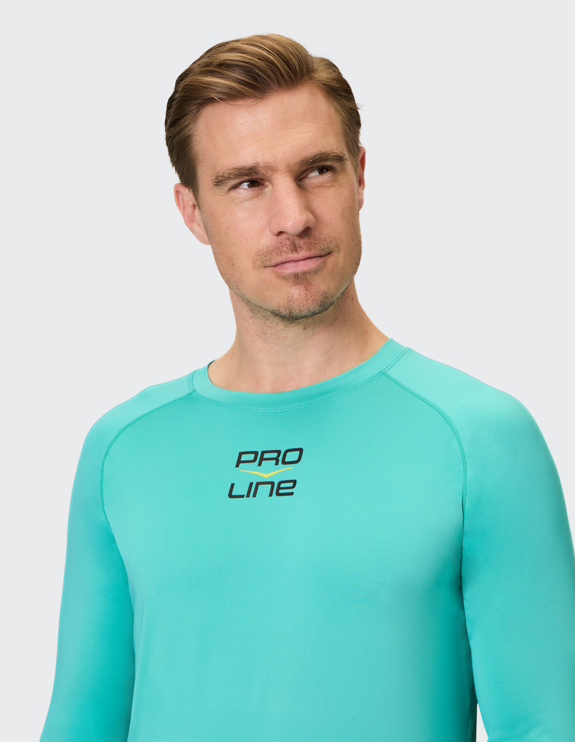 Ein Mann mit hellbraunem Haar trägt ein türkisfarbenes Langarmshirt mit "PRO LINE"-Aufdruck und blickt nachdenklich zur Seite.