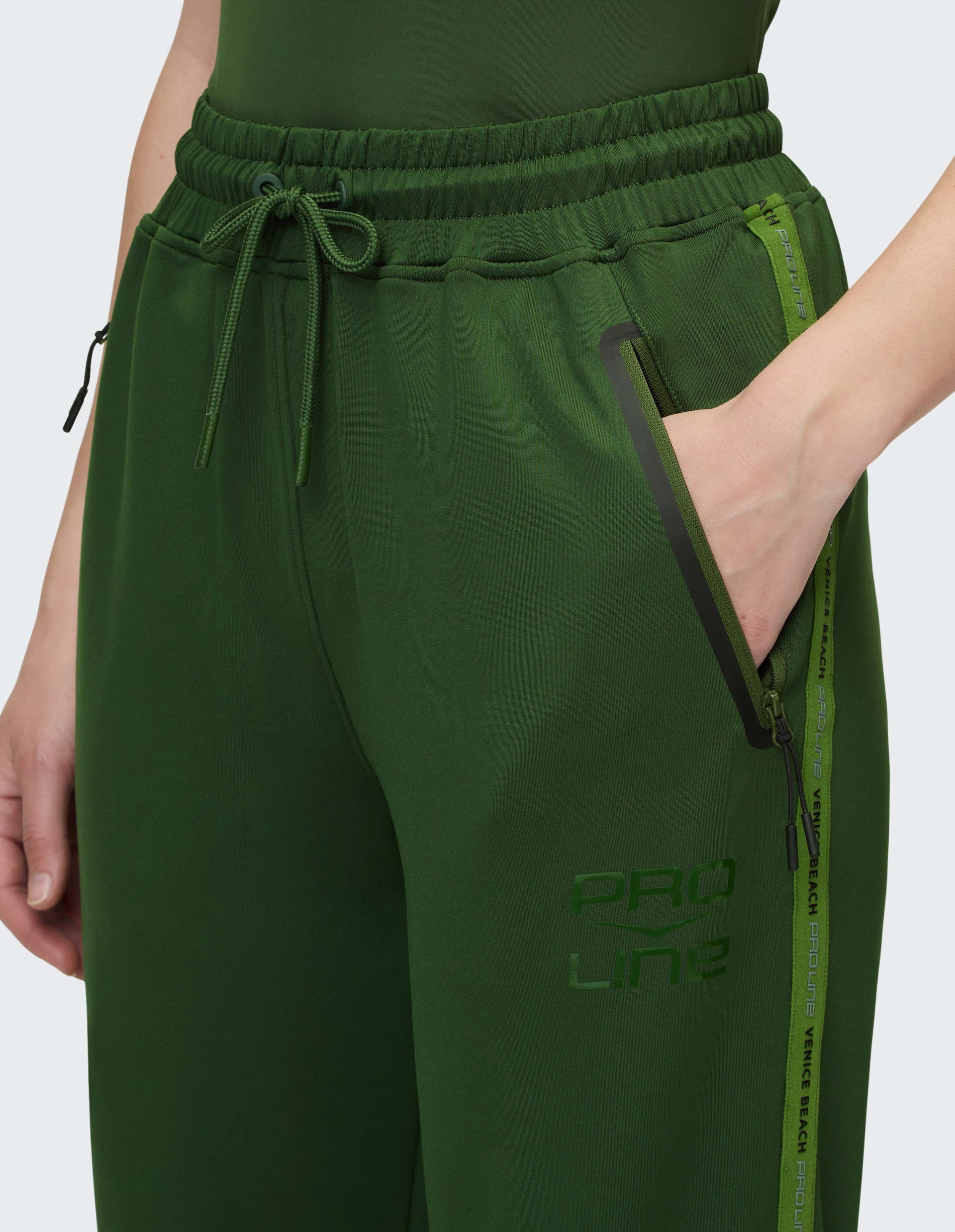 Person trägt grüne Jogginghose mit Kordelzug und Reißverschlusstaschen; Aufdruck PRO LINE über dem Knie sichtbar.