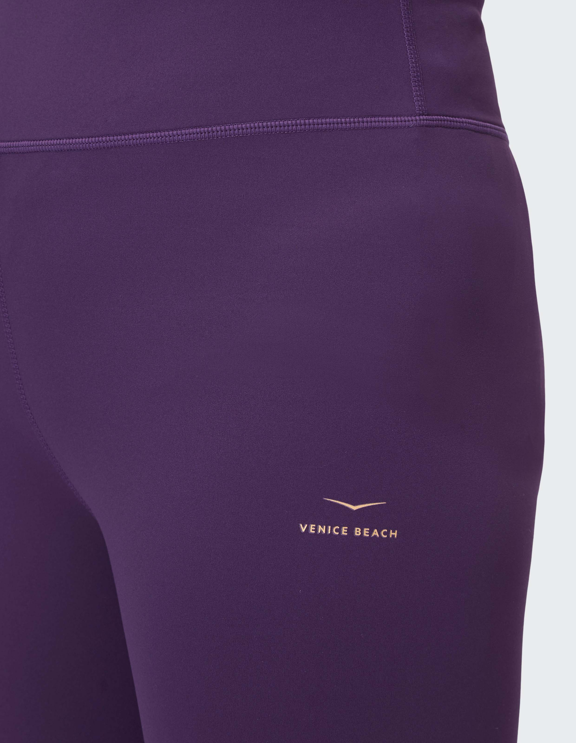 Lila Leggings aus glattem Stoff mit einem kleinen goldenen "Venice Beach"-Logo auf der rechten Hüfte, Nahaufnahme.