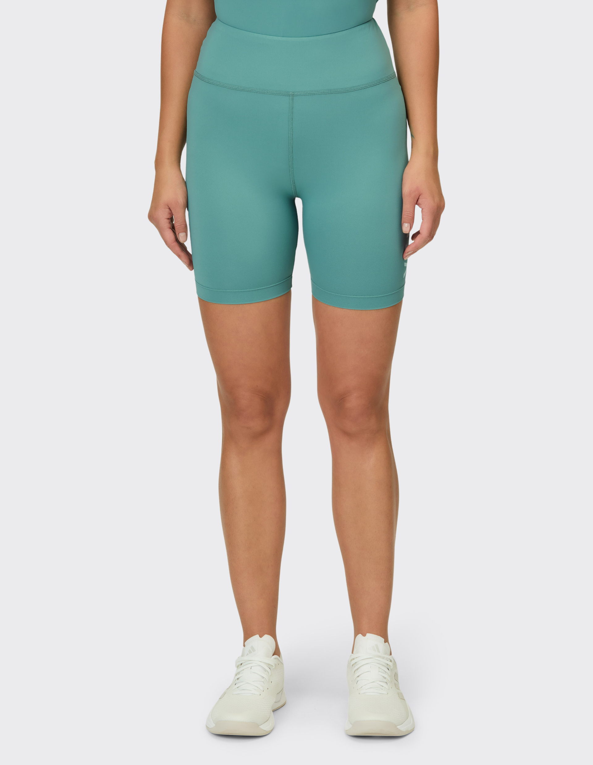 Eine Frau trägt hellgrüne Radlerhosen mit hohem Bund und weiße Turnschuhe.