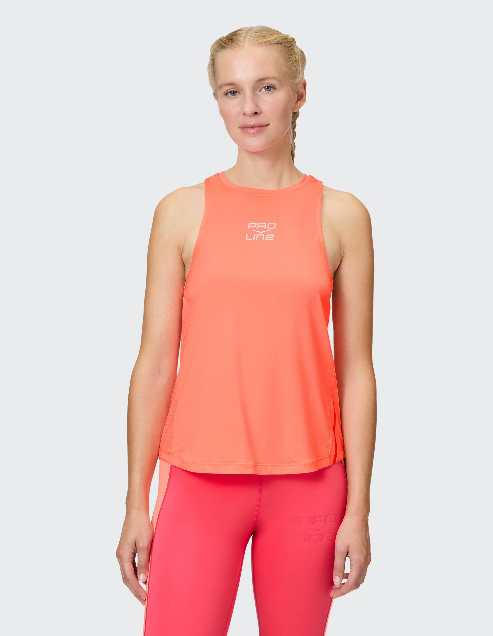 Eine Frau trägt ein neonorangenes Sporttop mit der Aufschrift PRO LINE und passende Leggings, stehend vor grauem Hintergrund.