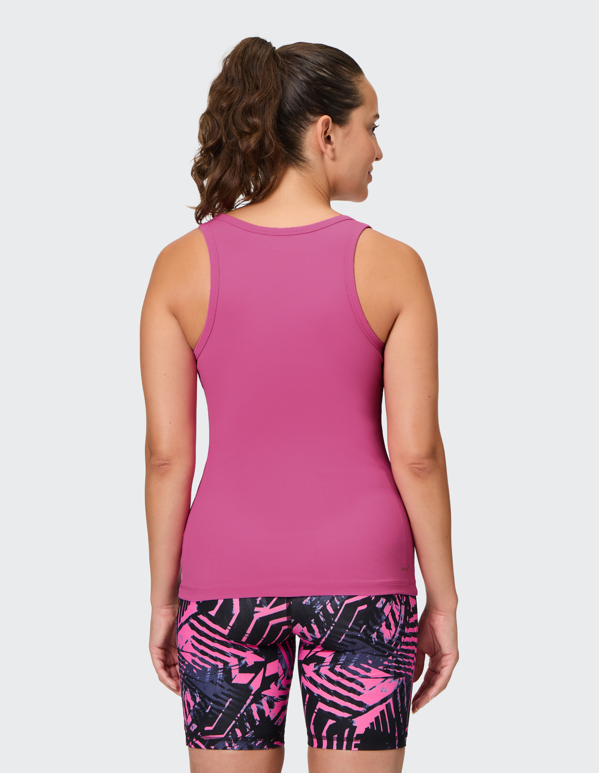 Eine Frau von hinten in einem pinken Tanktop und pink-schwarz gemusterten Shorts, trägt einen lockigen Pferdeschwanz.