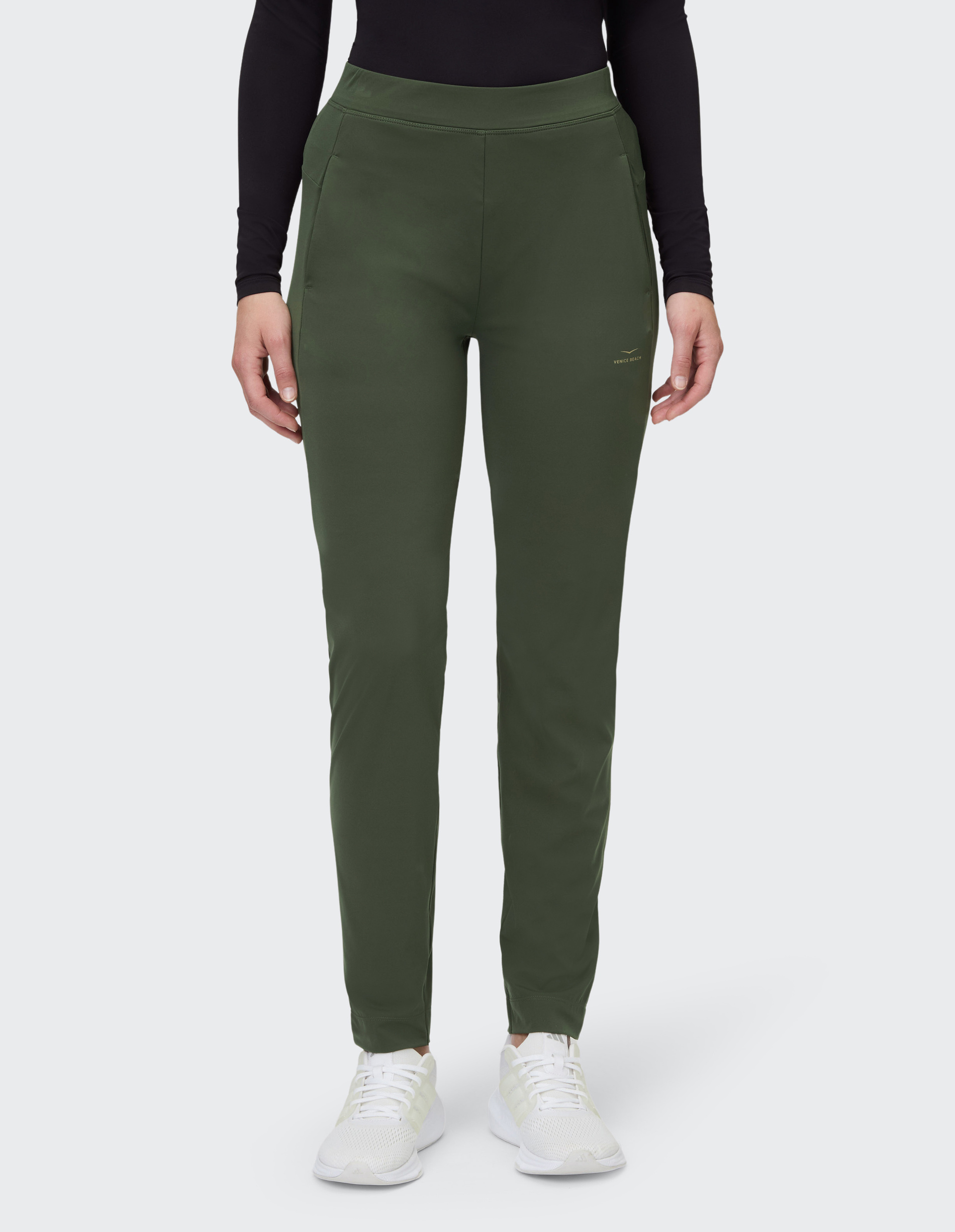 Person trägt eine olivgrüne Sporthose mit seitlichen Taschen und weißen Sportschuhen, kombiniert mit einem schwarzen Oberteil.