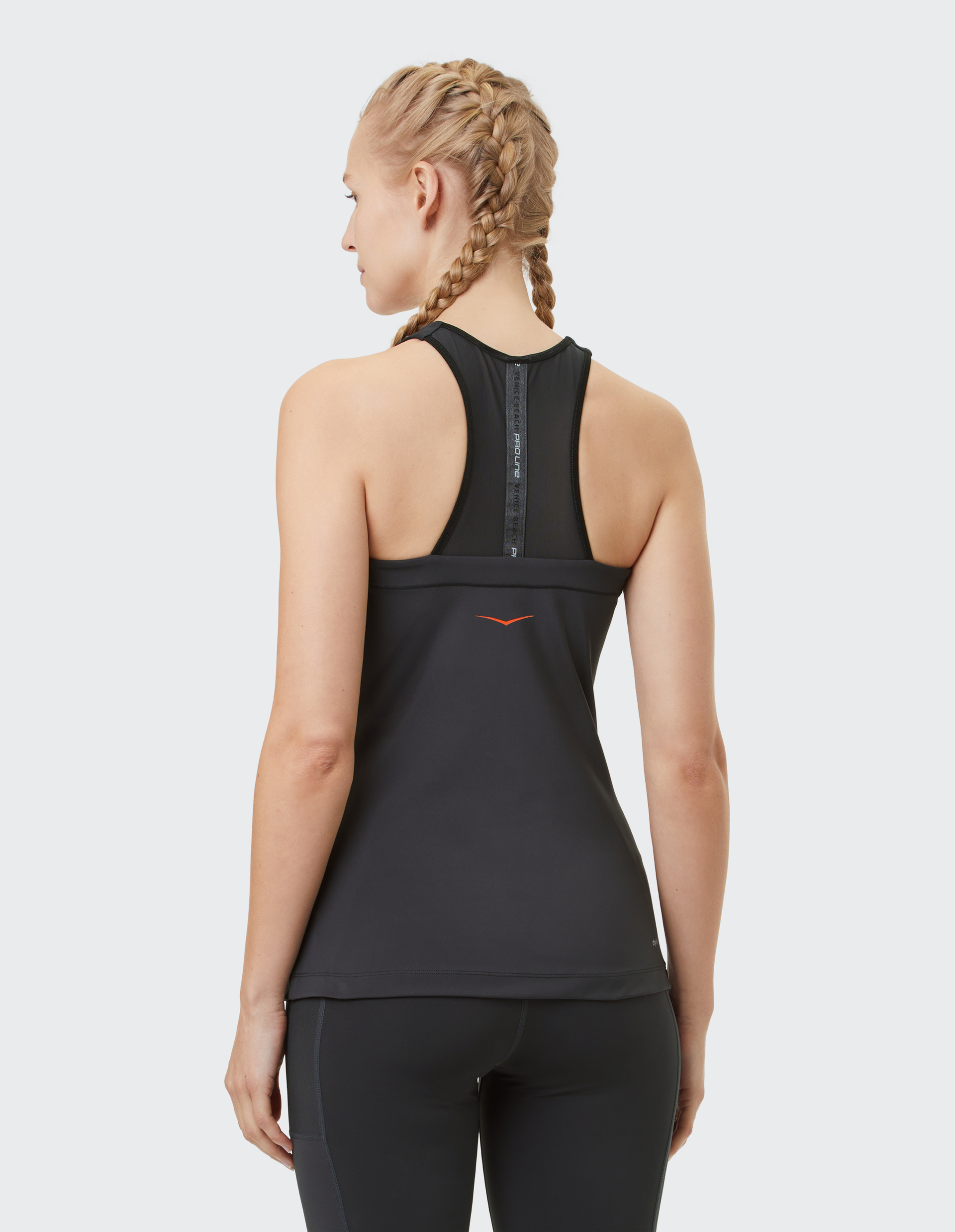 Eine Frau mit geflochtenem Haar trägt ein schwarzes Sporttop und -leggings, zeigt den Rücken mit einem kleinen orangefarbenen Logo.