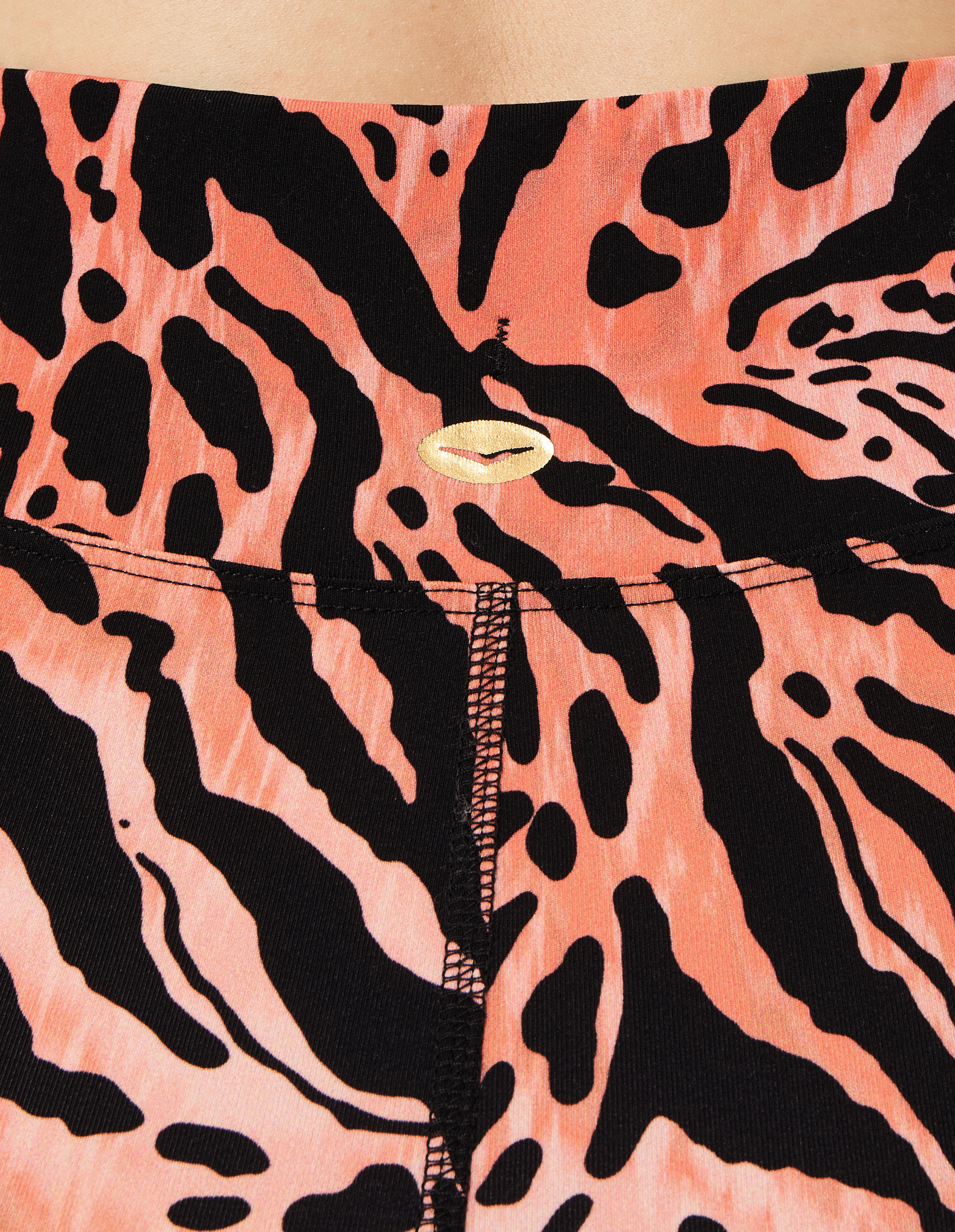 Nahaufnahme eines orange-schwarzen, wild gemusterten Stoffes mit goldfarbenem Emblem und einer vertikalen Naht in der Mitte.