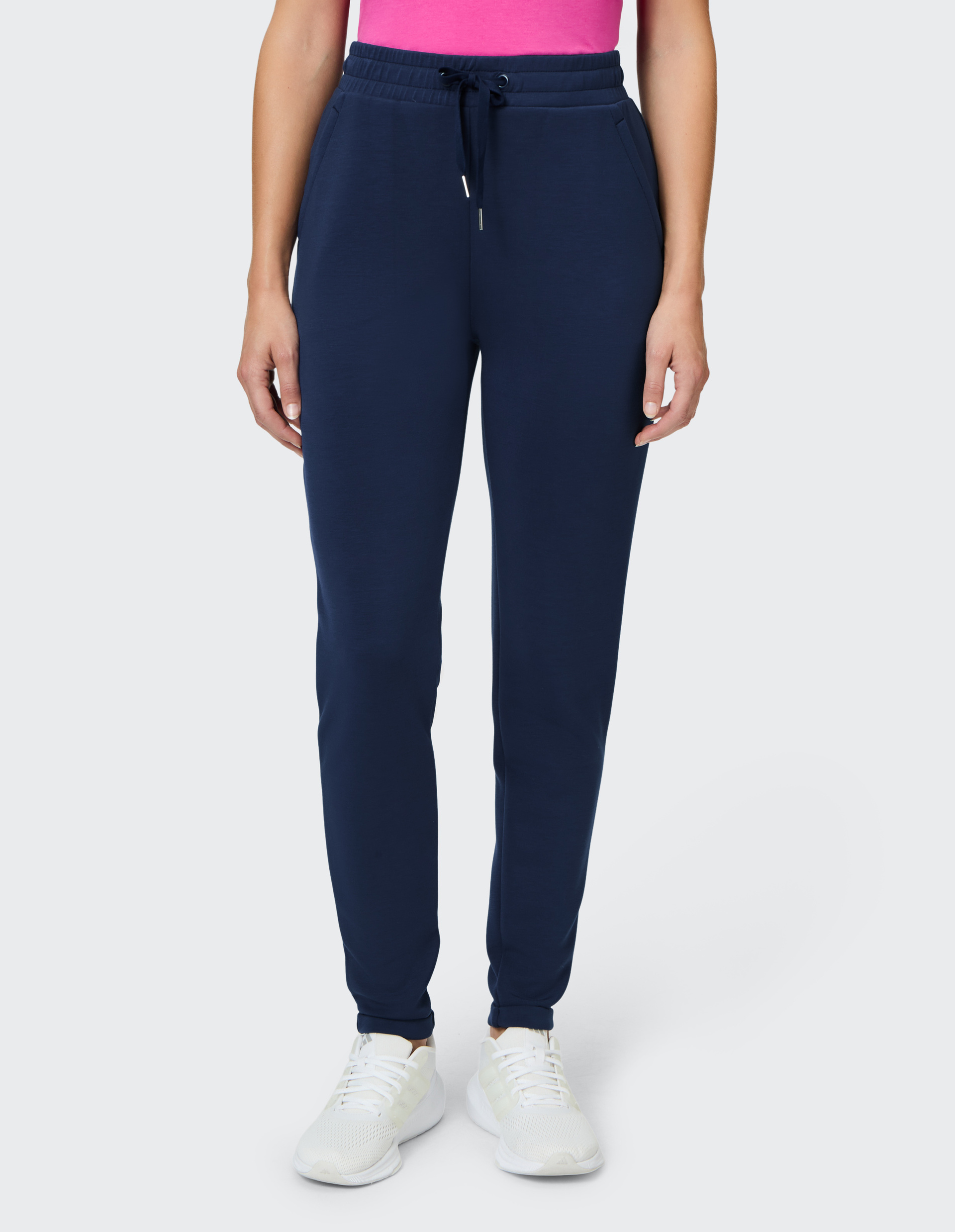 Frau trägt dunkelblaue Jogginghose mit Kordelzug und weiße Sneakers, kombiniert mit einem leuchtend pinken Oberteil.