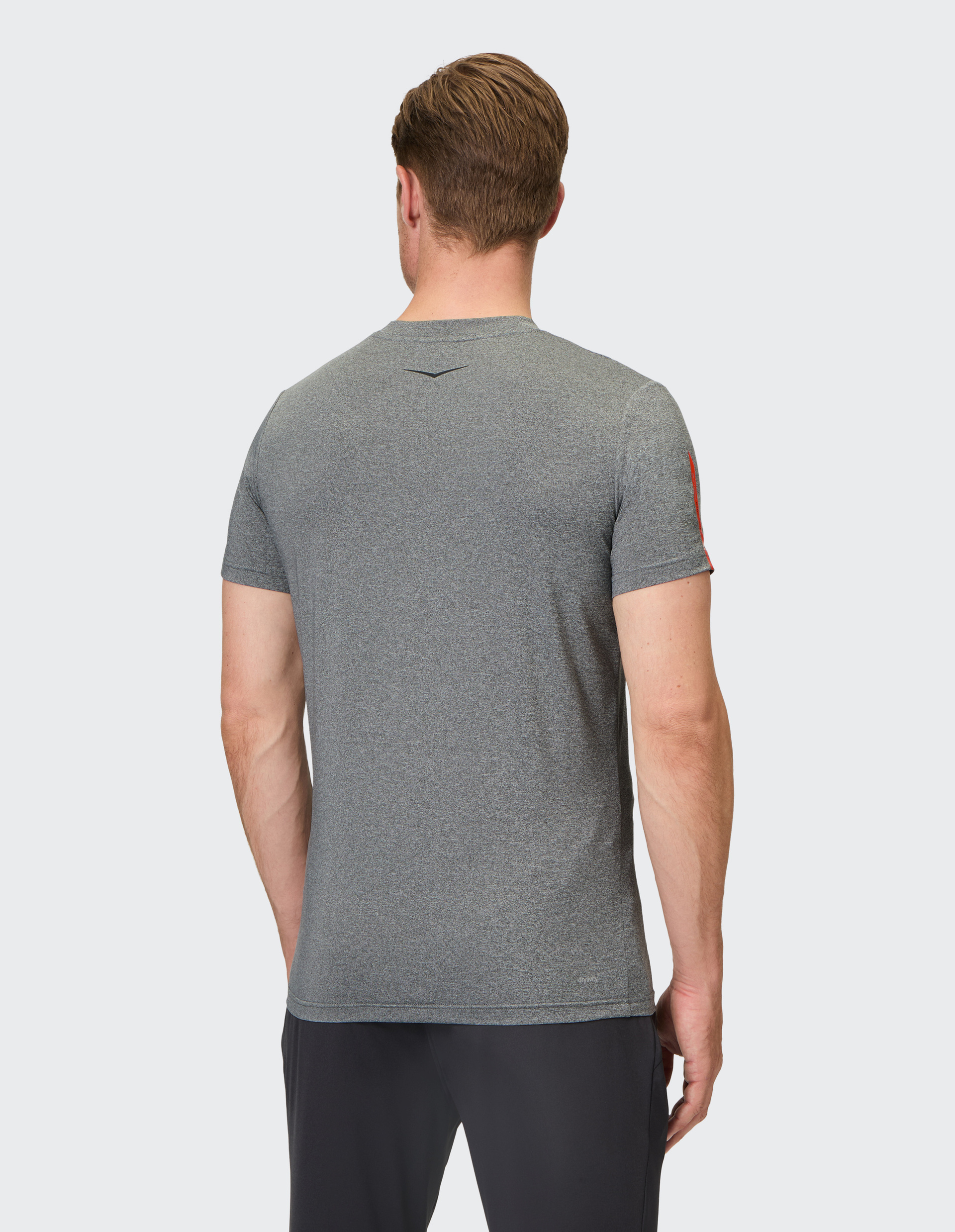 Ein Mann trägt ein graues T-Shirt und schwarze Hosen, fotografiert von hinten vor einem hellgrauen Hintergrund.