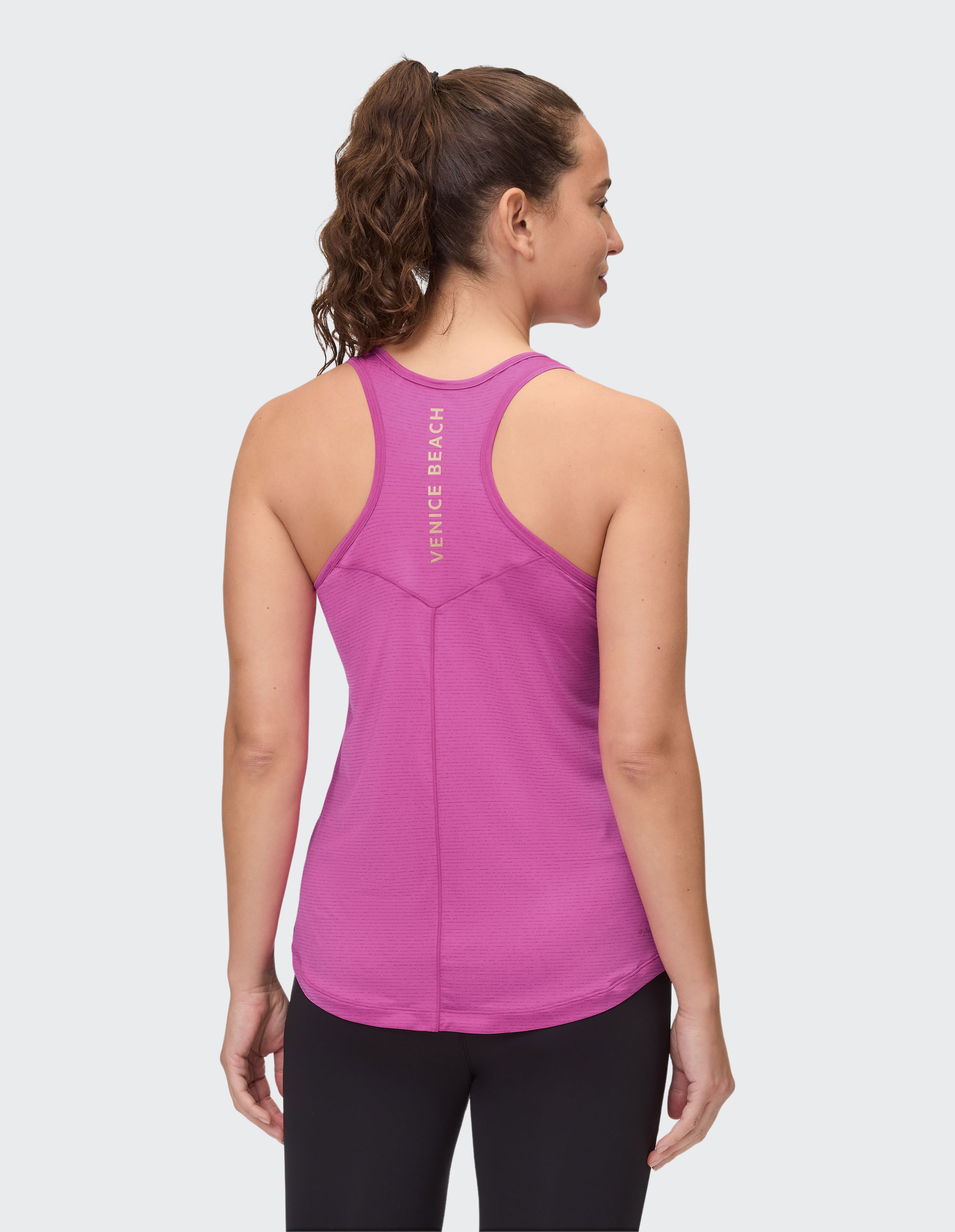 Frau mit einem rosa Racerback-Top mit "Venice Beach" auf dem Rücken, trägt eine schwarze Hose und hat einen Pferdeschwanz.