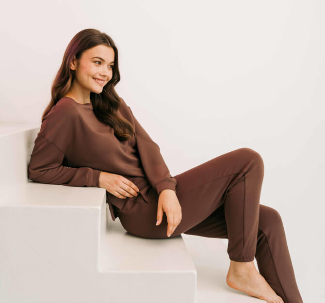 Auf einer Treppe sitzenden Frau im braunen Homewear-Anzug.