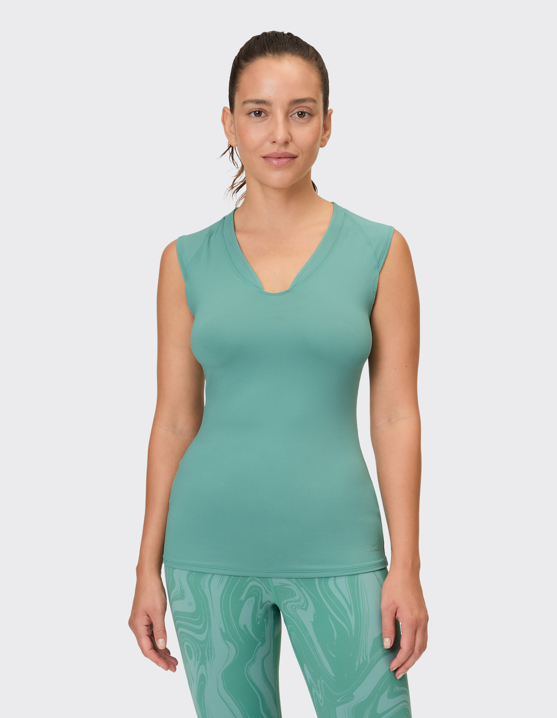 Eine Frau trägt ein mintgrünes Top mit V-Ausschnitt und eine Leggings mit grünem Marmormuster.