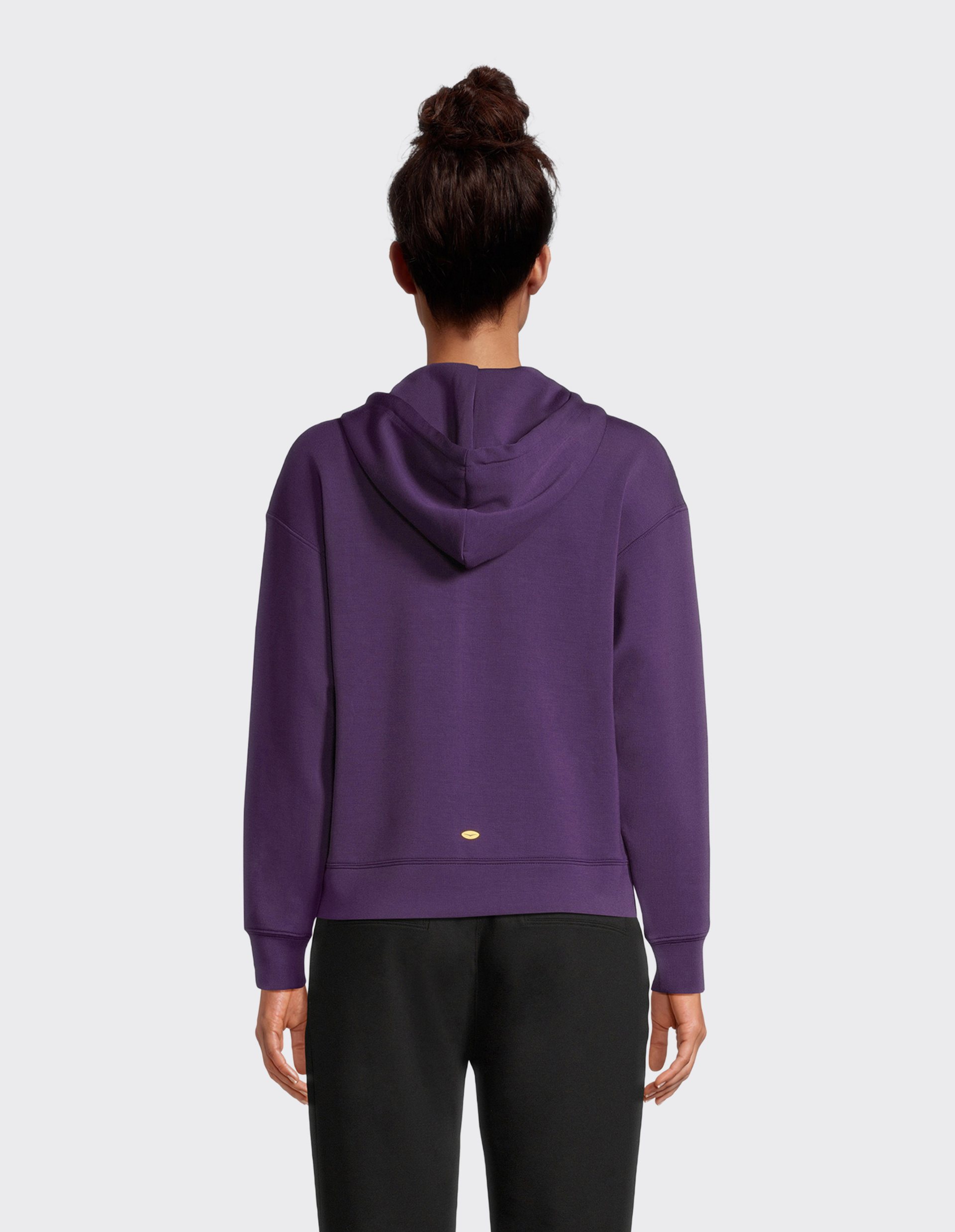 Rückenansicht einer Frau in einem violetten Kapuzenpullover mit Kapuze und einem kleinen goldenen Oval auf der Rückseite.