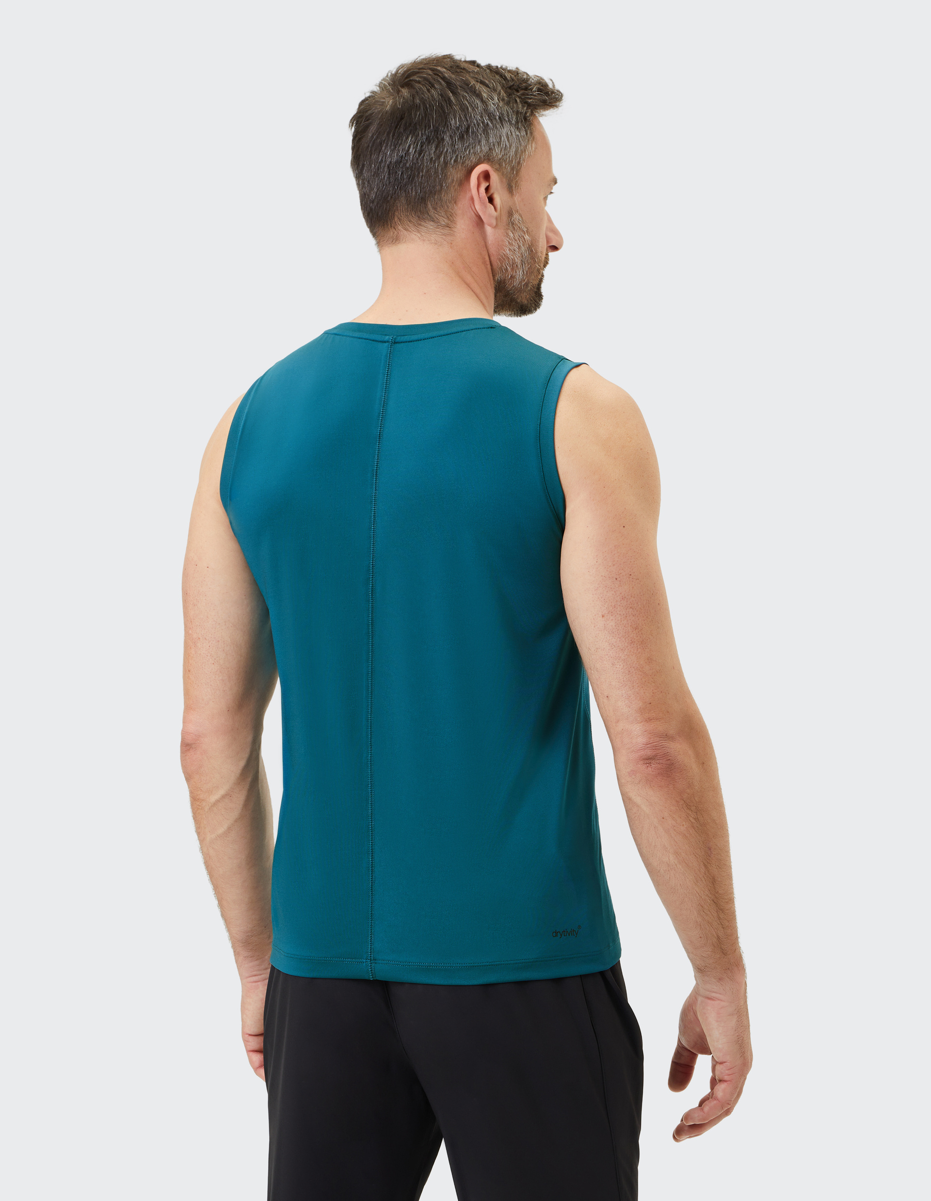 Mann mit kurzem Haar von hinten in ärmellosem, petrolfarbenem Sportshirt und schwarzer Hose vor weißem Hintergrund.