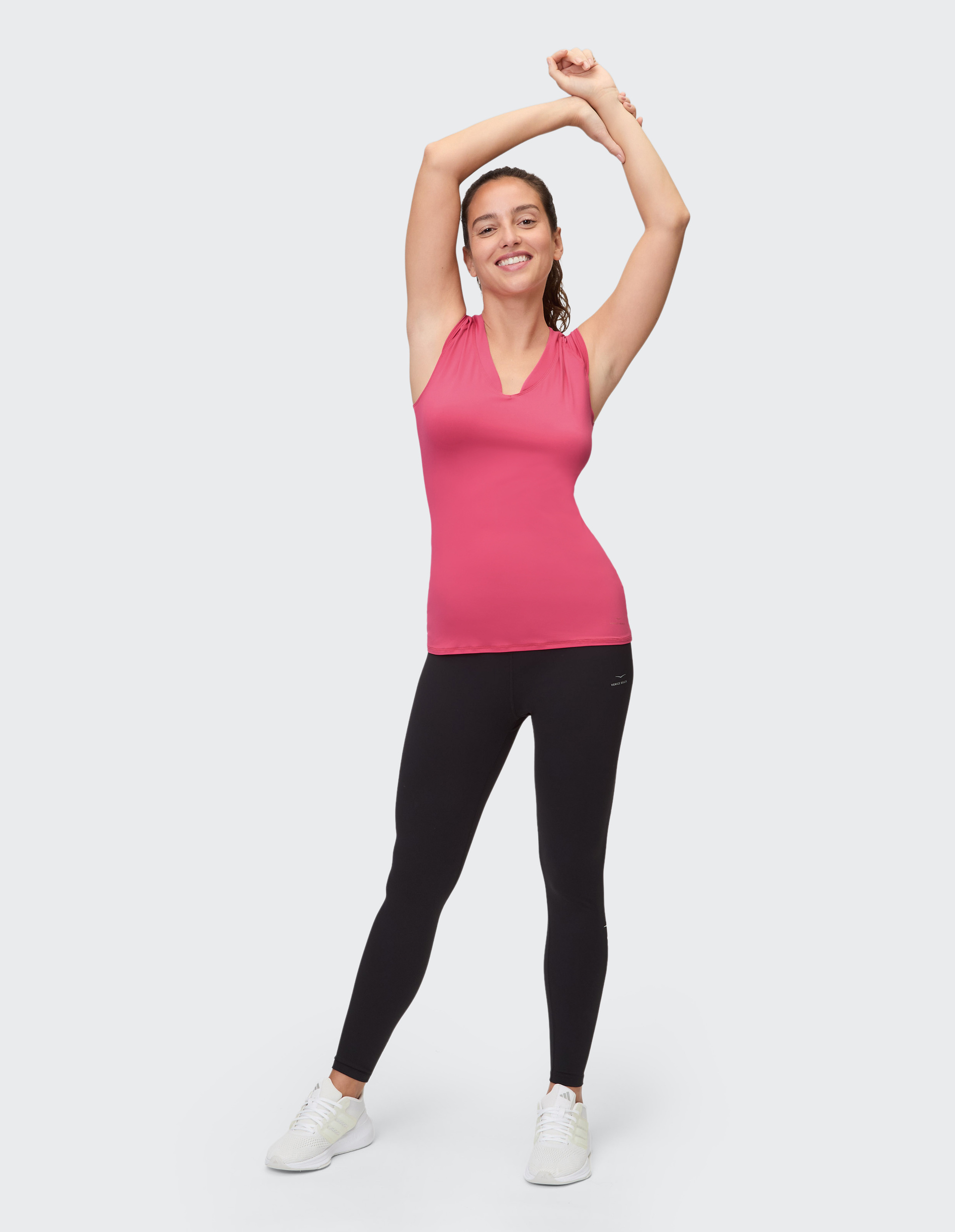Frau in einem schmalen, schillernden pinkfarbenen Sportoberteil mit V-Ausschnitt und schwarzen Leggings.