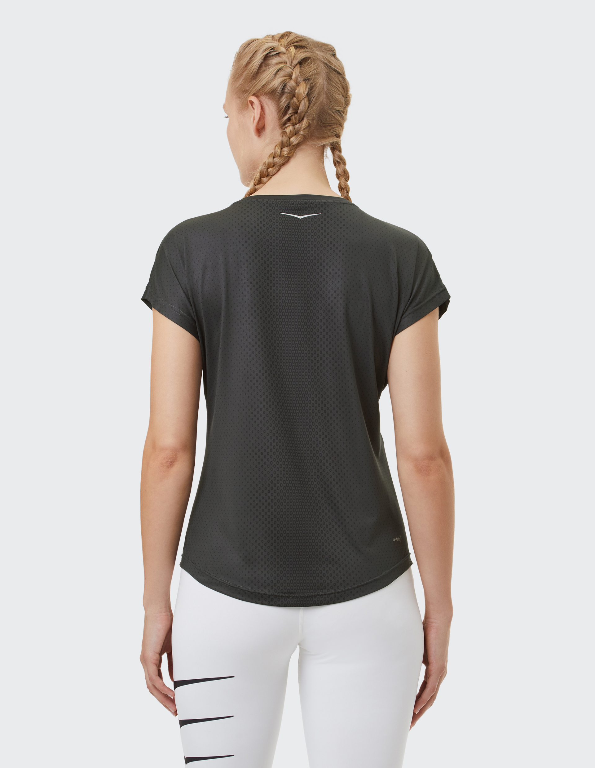 Frau mit Zopf und geflochtenem Haar in schwarzem Sportoberteil und weißen Leggings mit schwarzem Muster, rückseitig fotografiert.