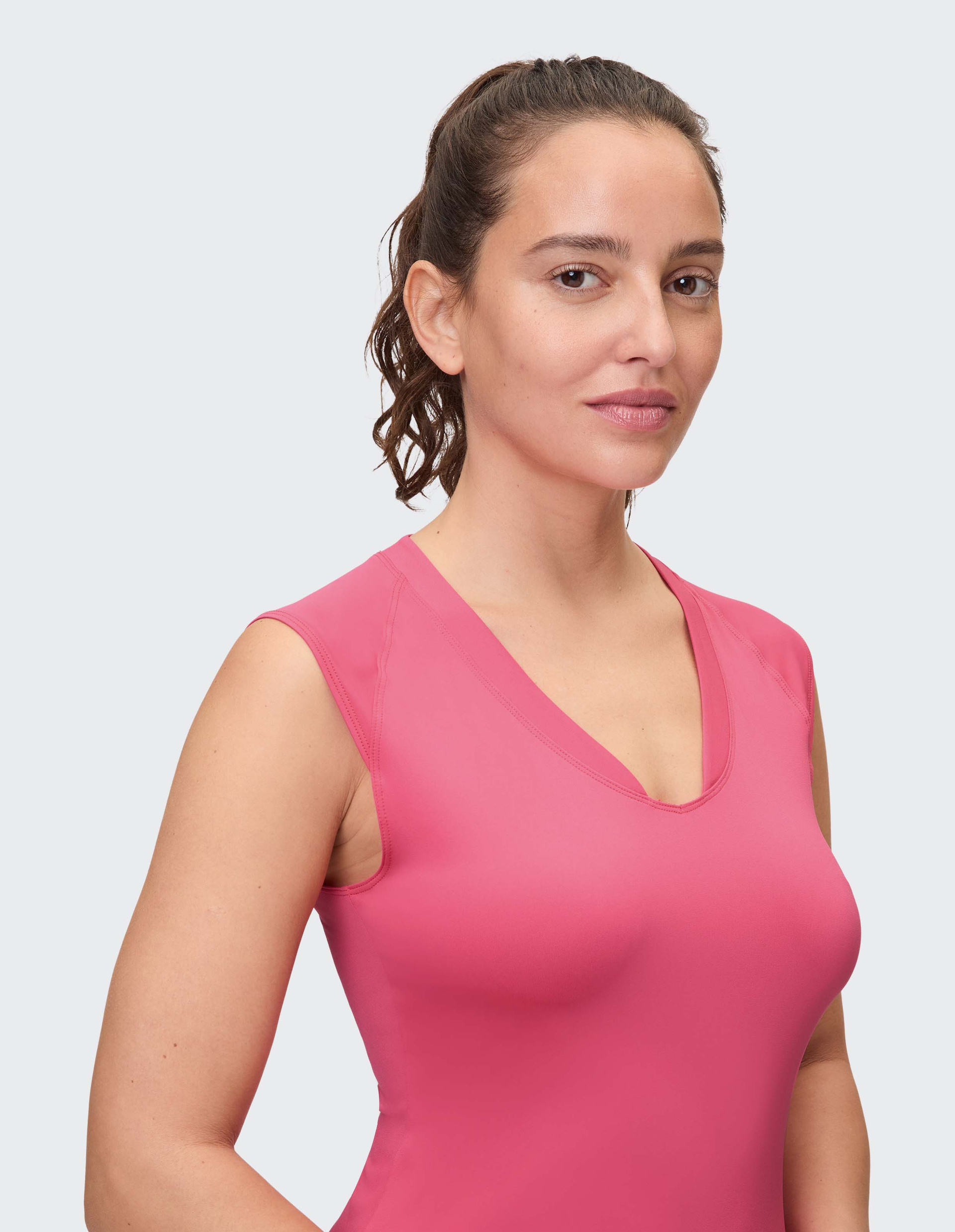 Eine Frau mit dunklen Haaren trägt ein ärmelloses pinkes Oberteil mit V-Ausschnitt.